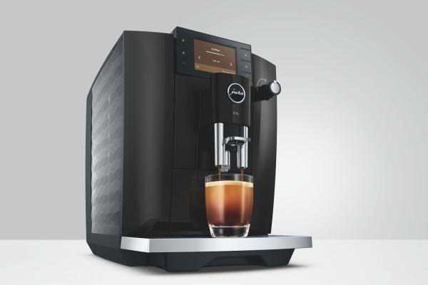 Eine schwarze Kaffeemaschine brüht Kaffee in ein Glas mit braunem Schaum.