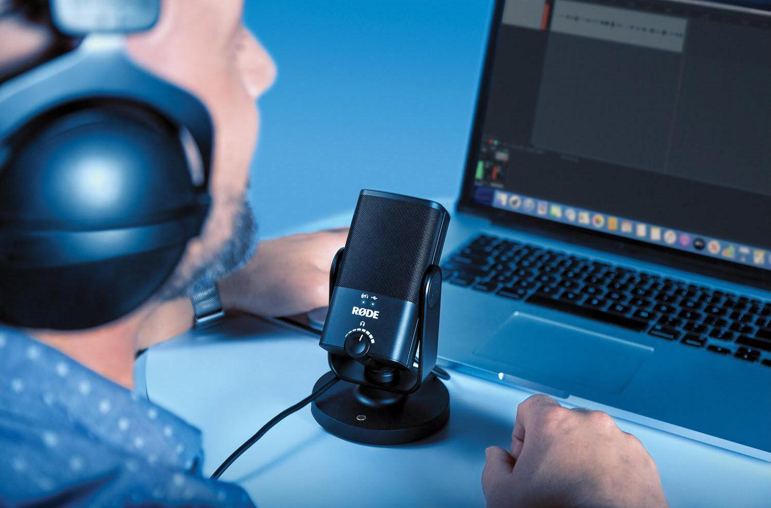Uomo con cuffie parla in un microfono di fronte a un laptop.