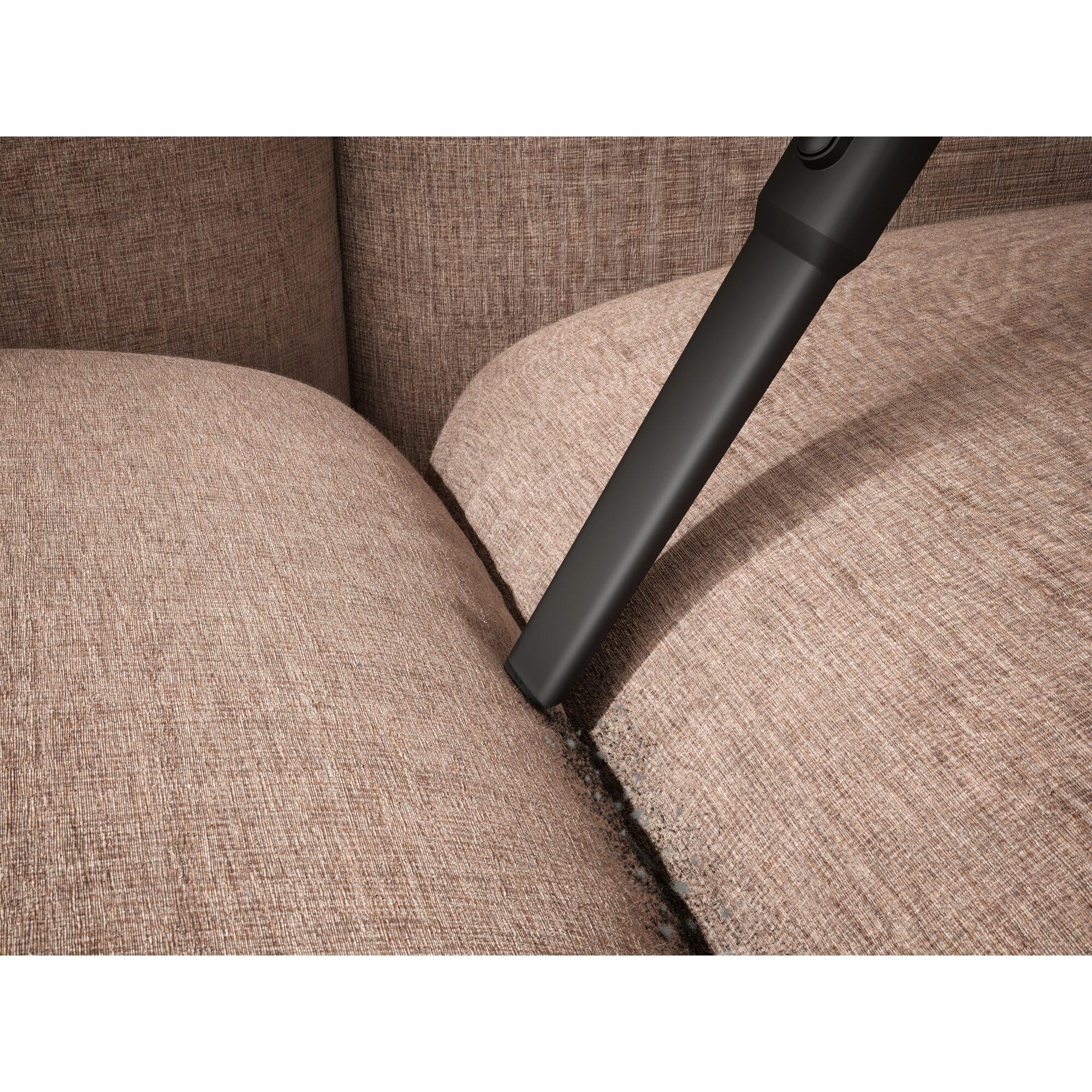 Ein schwarzer Staubsaugeraufsatz reinigt eine braune Couch.