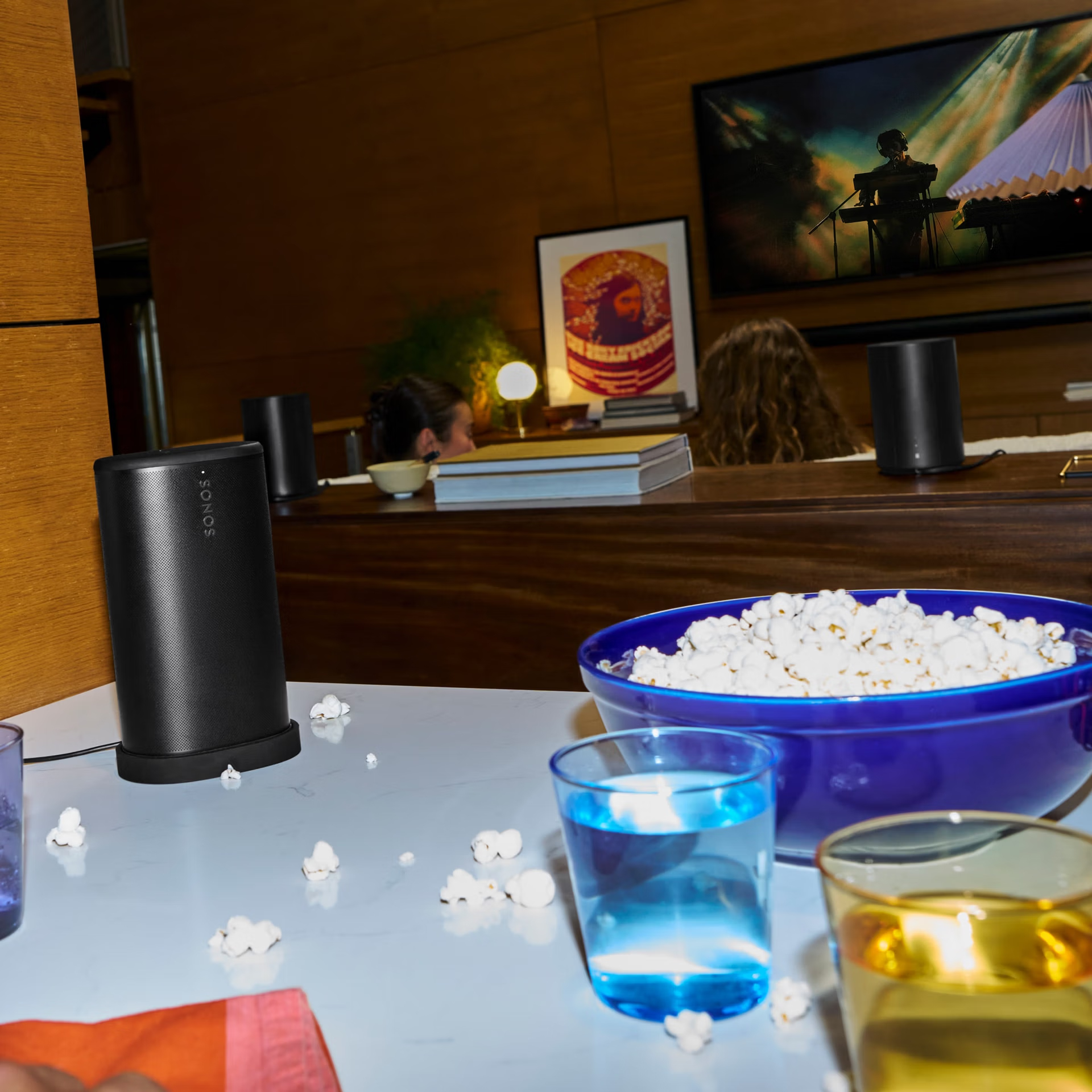 Czarny głośnik, popcorn, napoje i telewizor z muzykiem.