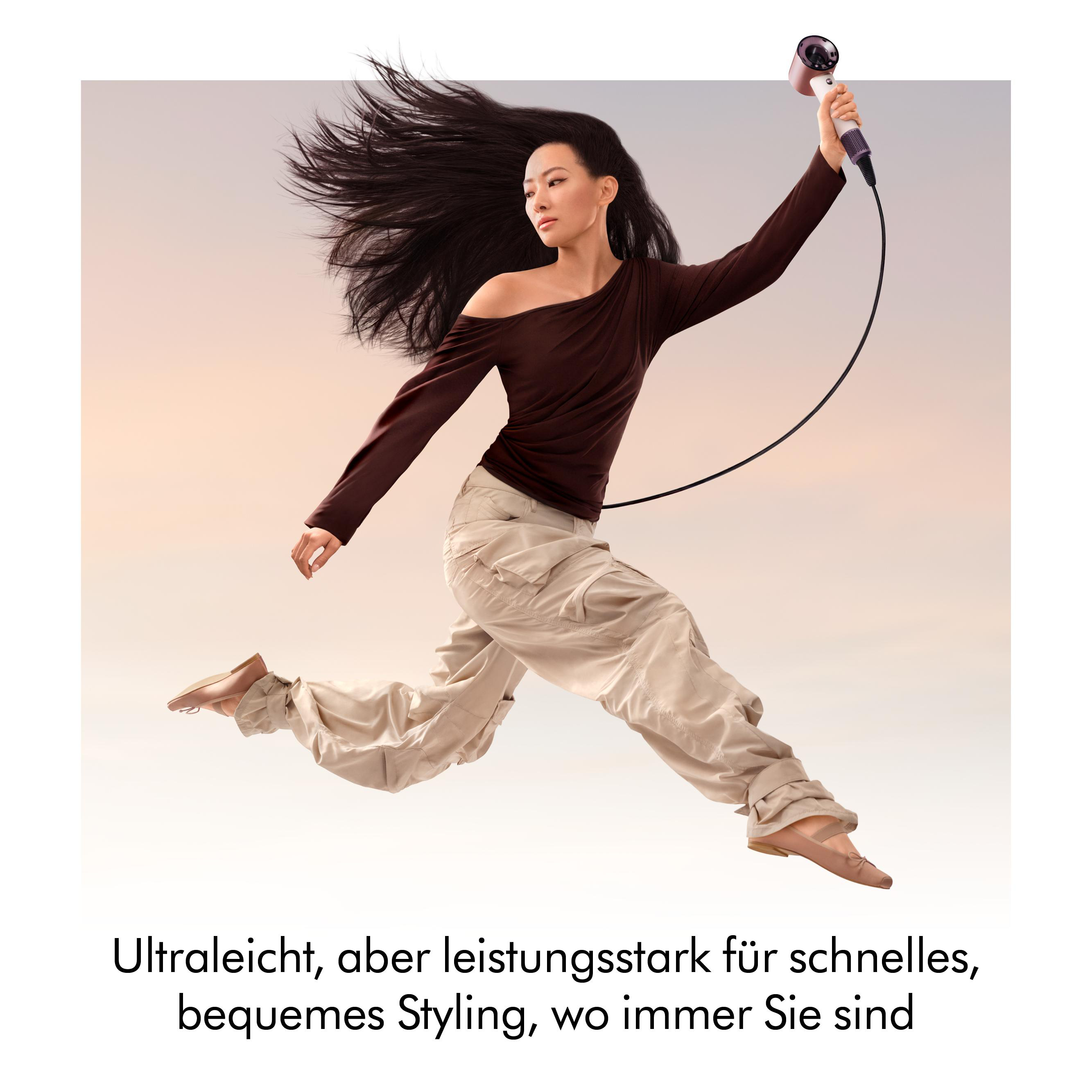 Frau mit langen Haaren und Reisehaartrockner springt.