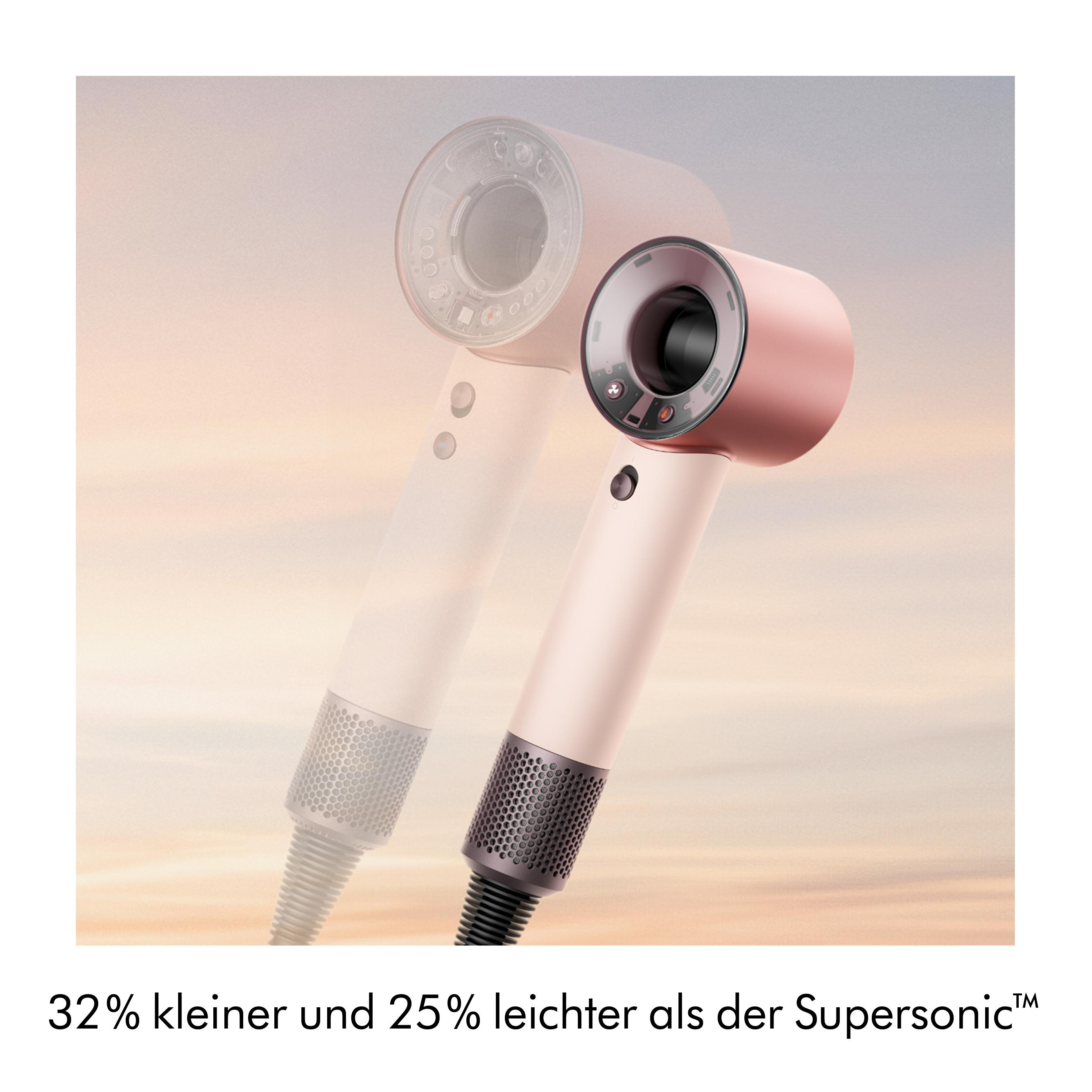 Ein rosafarbener Haartrockner mit schwarzem Diffusor vor einem verwaschenen Himmel.