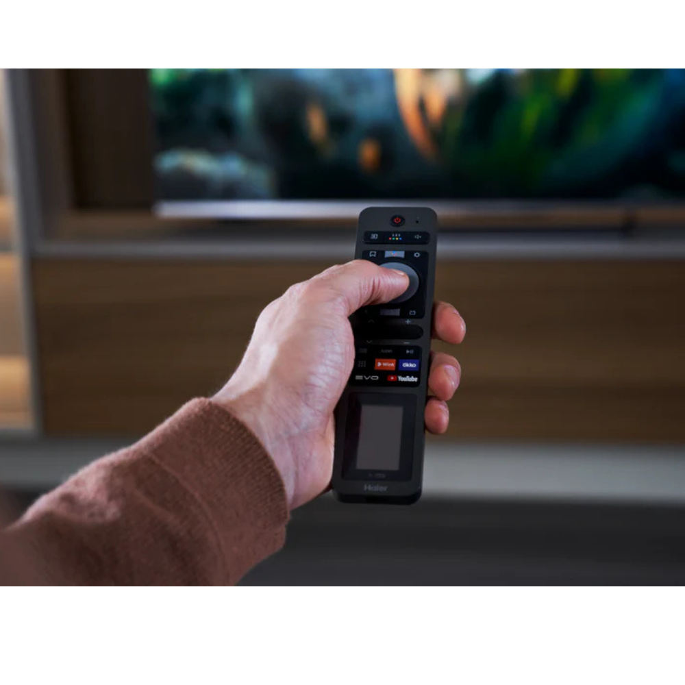 Una mano sostiene un mando a distancia frente a una pantalla de televisión borrosa.
