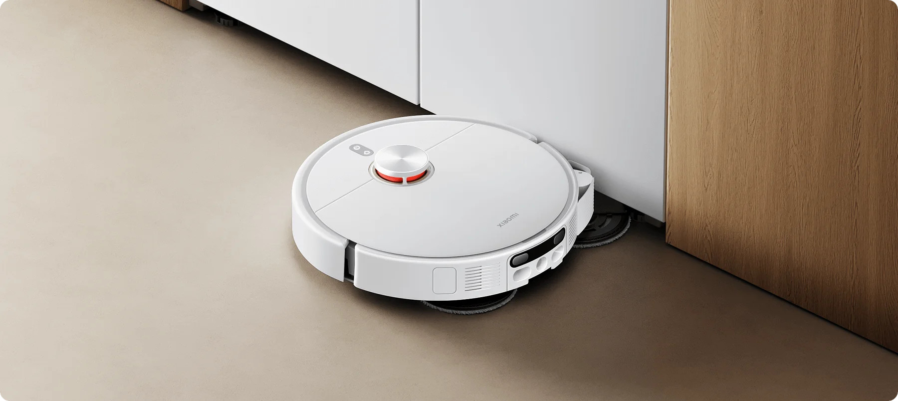 Biały robot sprzątający czyści podłogę obok drewnianej szafki.