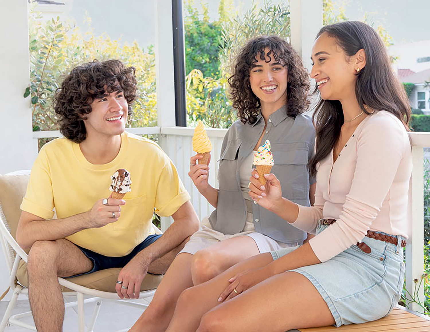 Tres jóvenes sentados afuera comiendo helado. El hombre de la izquierda tiene pelo rizado oscuro.