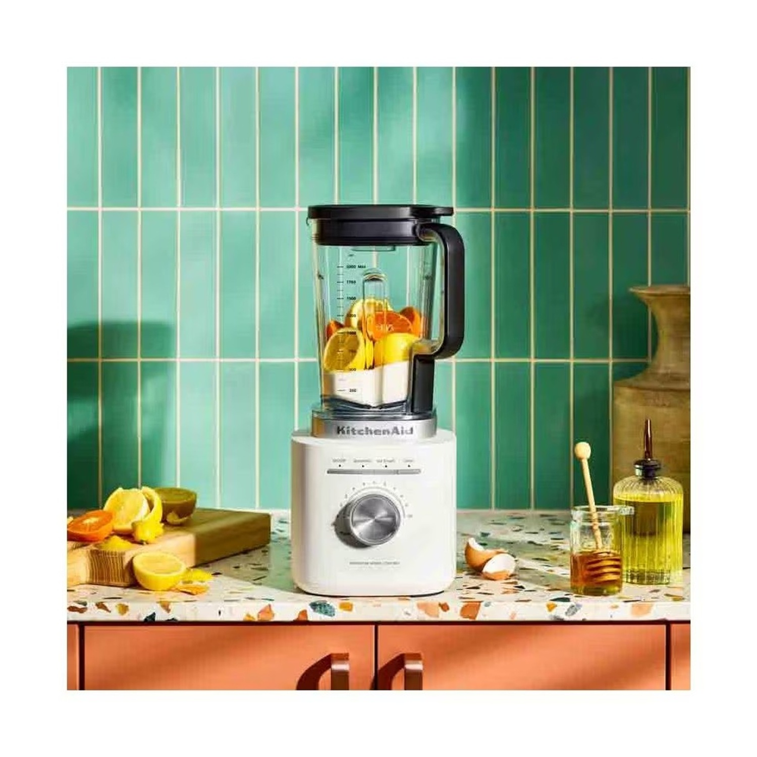 Un frullatore bianco con frutta e miele su un bancone da cucina.