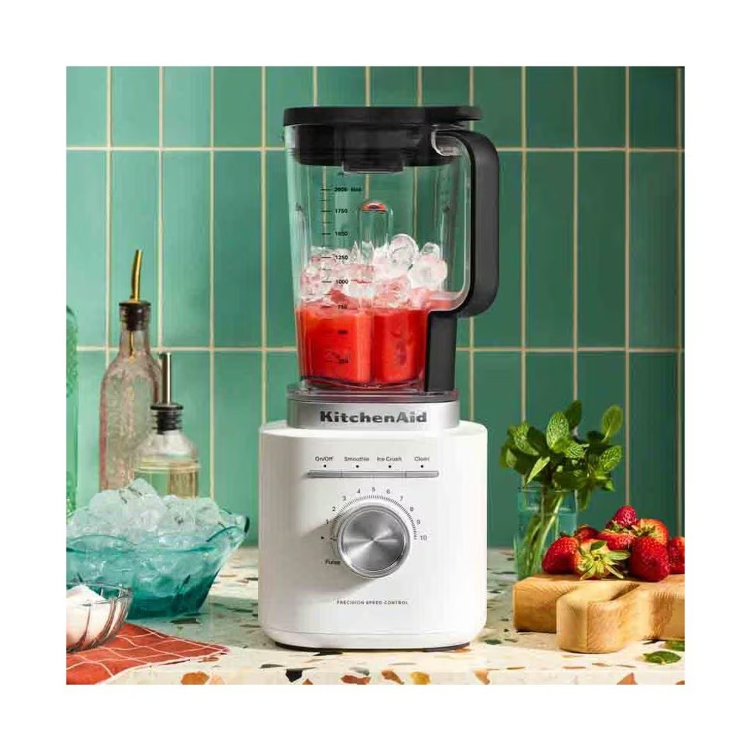 Un frullatore KitchenAid bianco con succo rosso e ghiaccio in un barattolo su un tavolo.