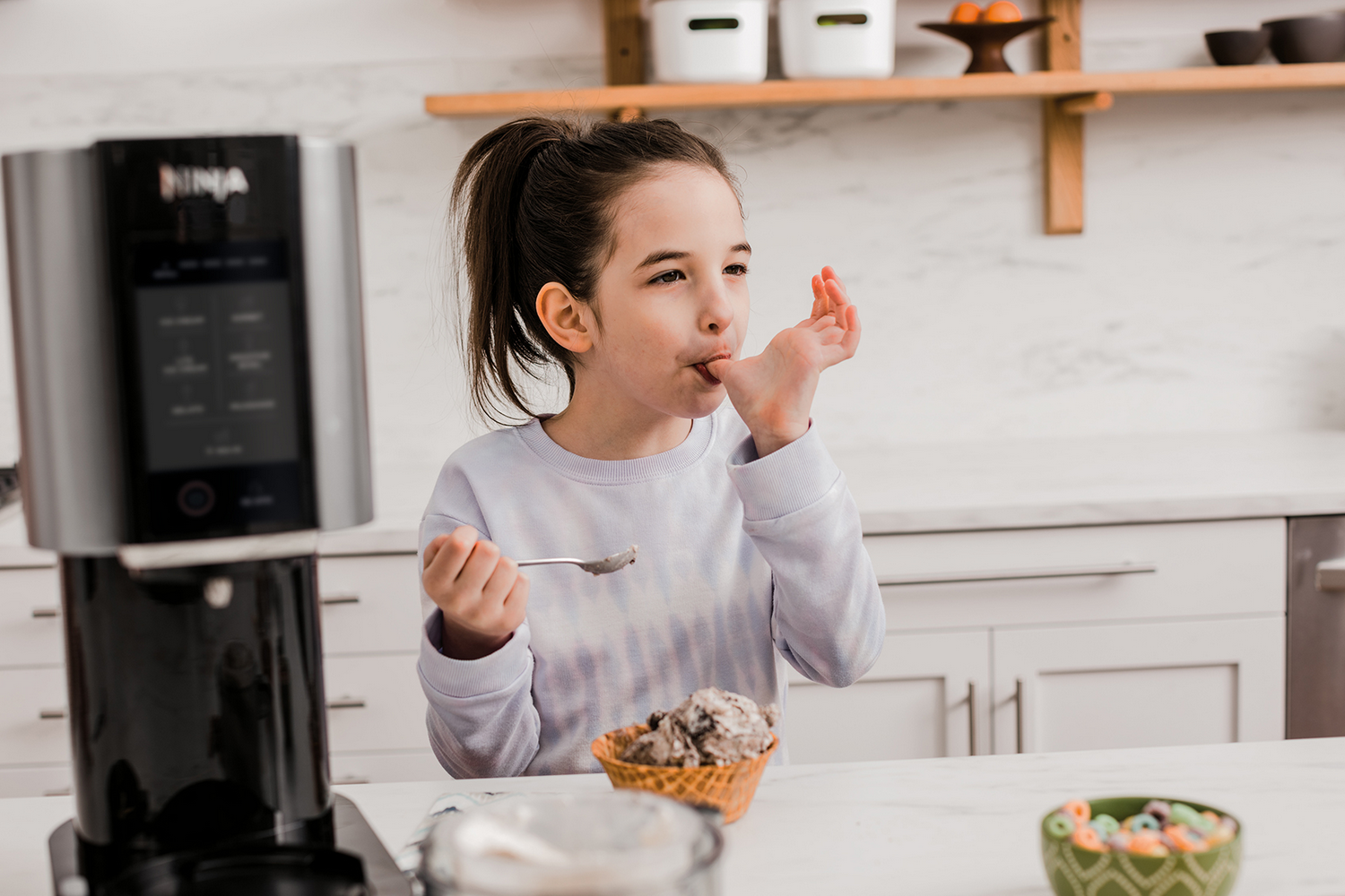 Una niña come helado de un cono de gofre en una cocina.
