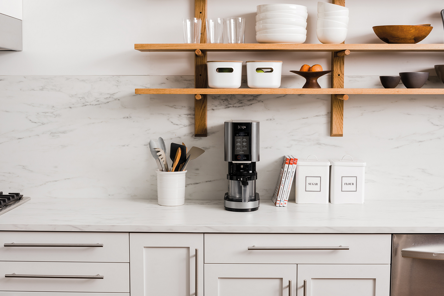 Una cafetera se asienta sobre una encimera de mármol con utensilios, botes y libros.