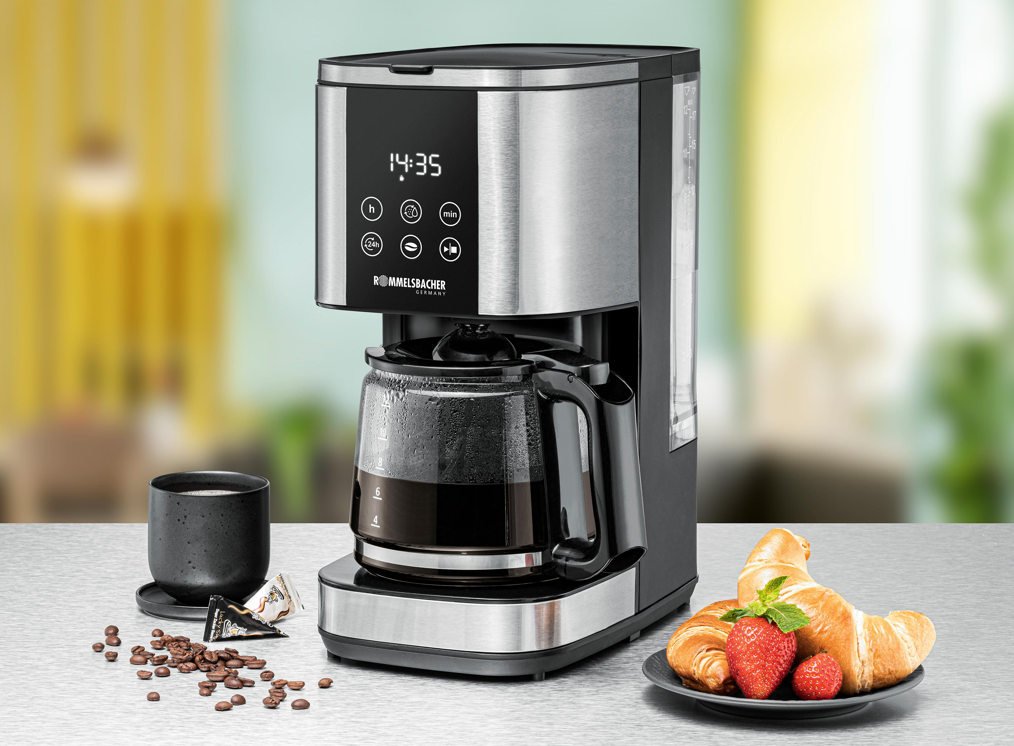 Kaffeemaschine mit Kanne, Tasse, Bohnen und Croissants auf dem Tisch.
