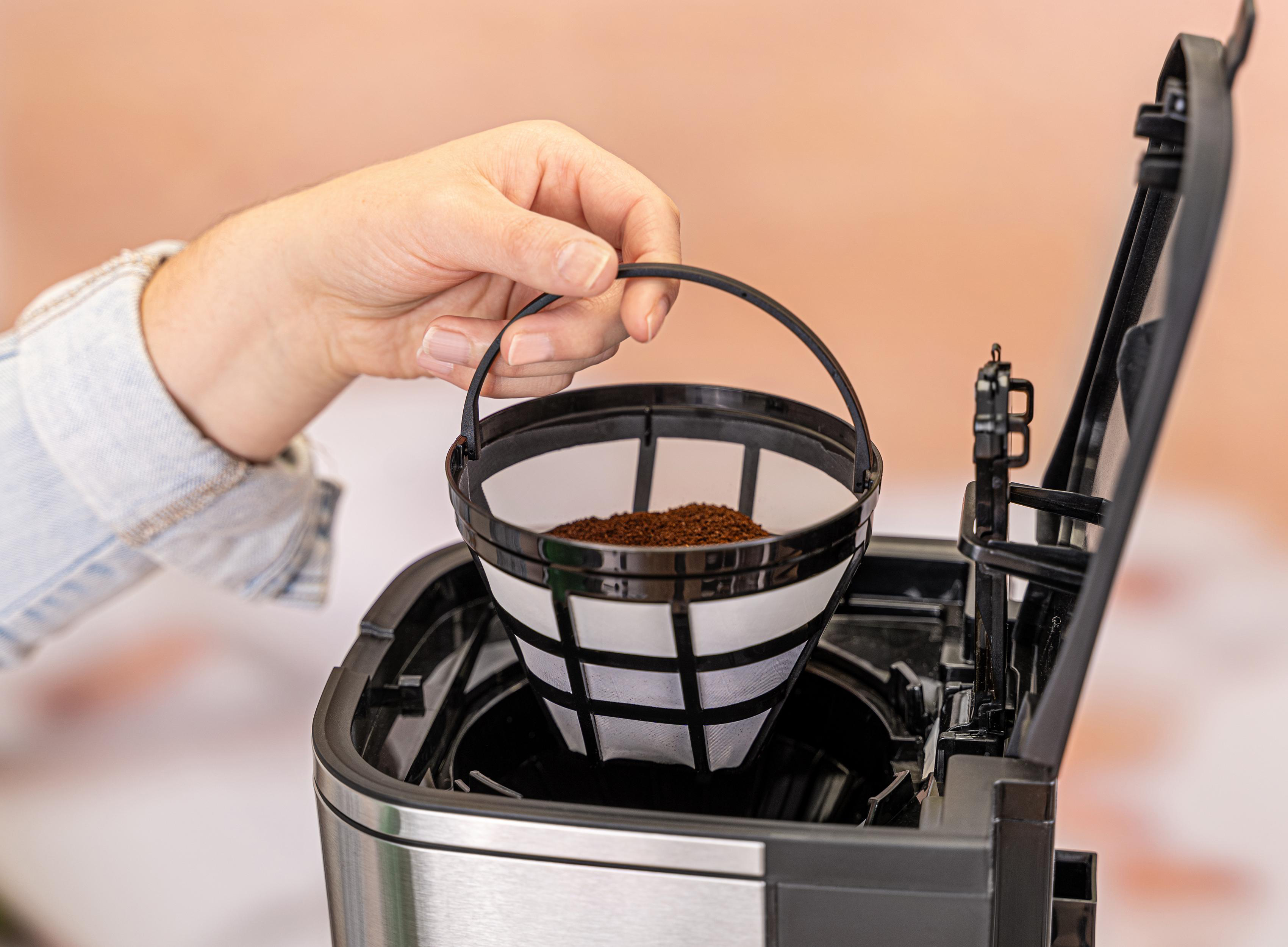 Eine Hand hält einen Kaffeefilter mit gemahlenem Kaffee in einer Kaffeemaschine.