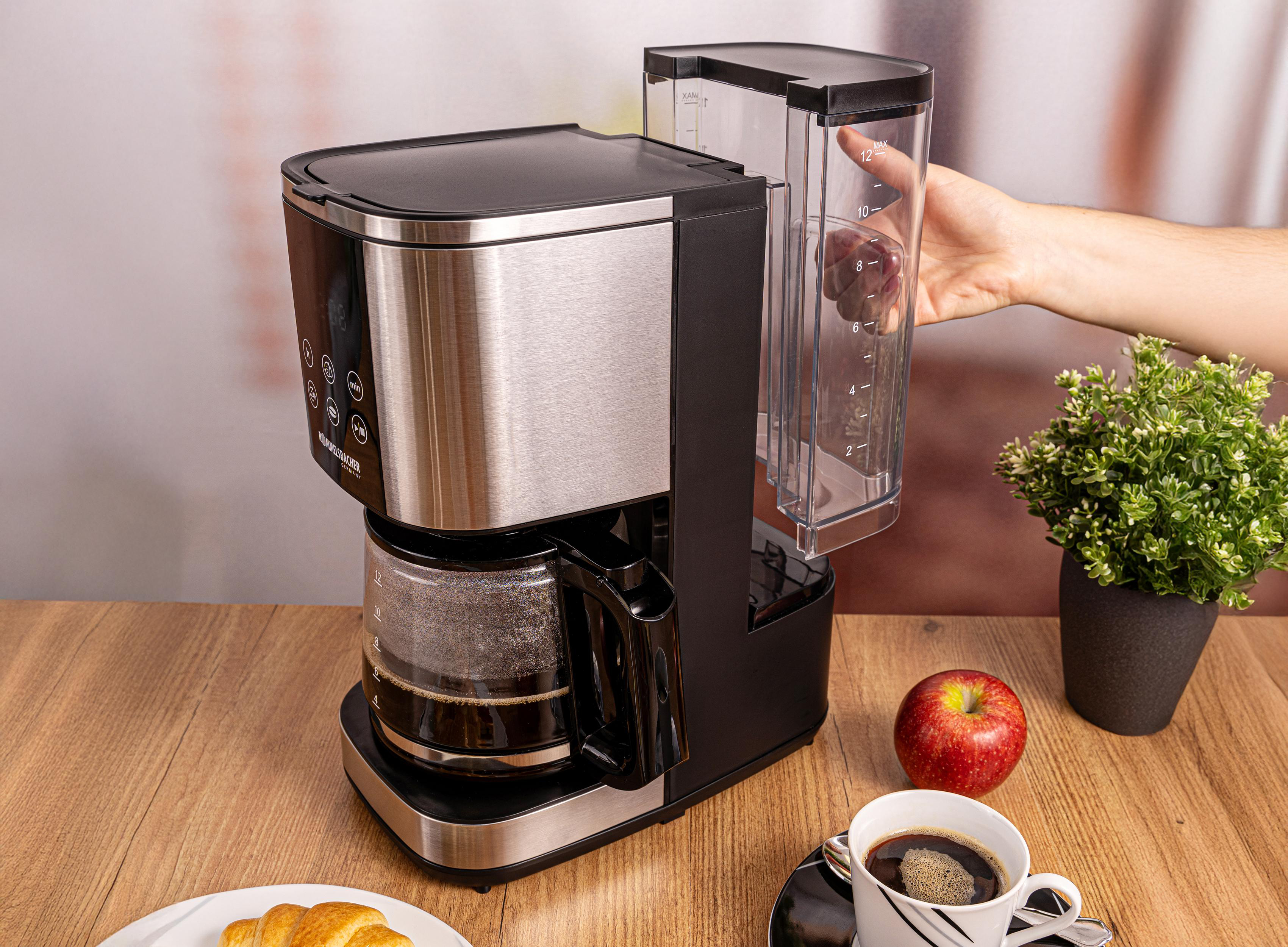 Kaffeemaschine mit Glaskanne, gefüllt mit Kaffee, daneben Apfel und Kaffeetasse.