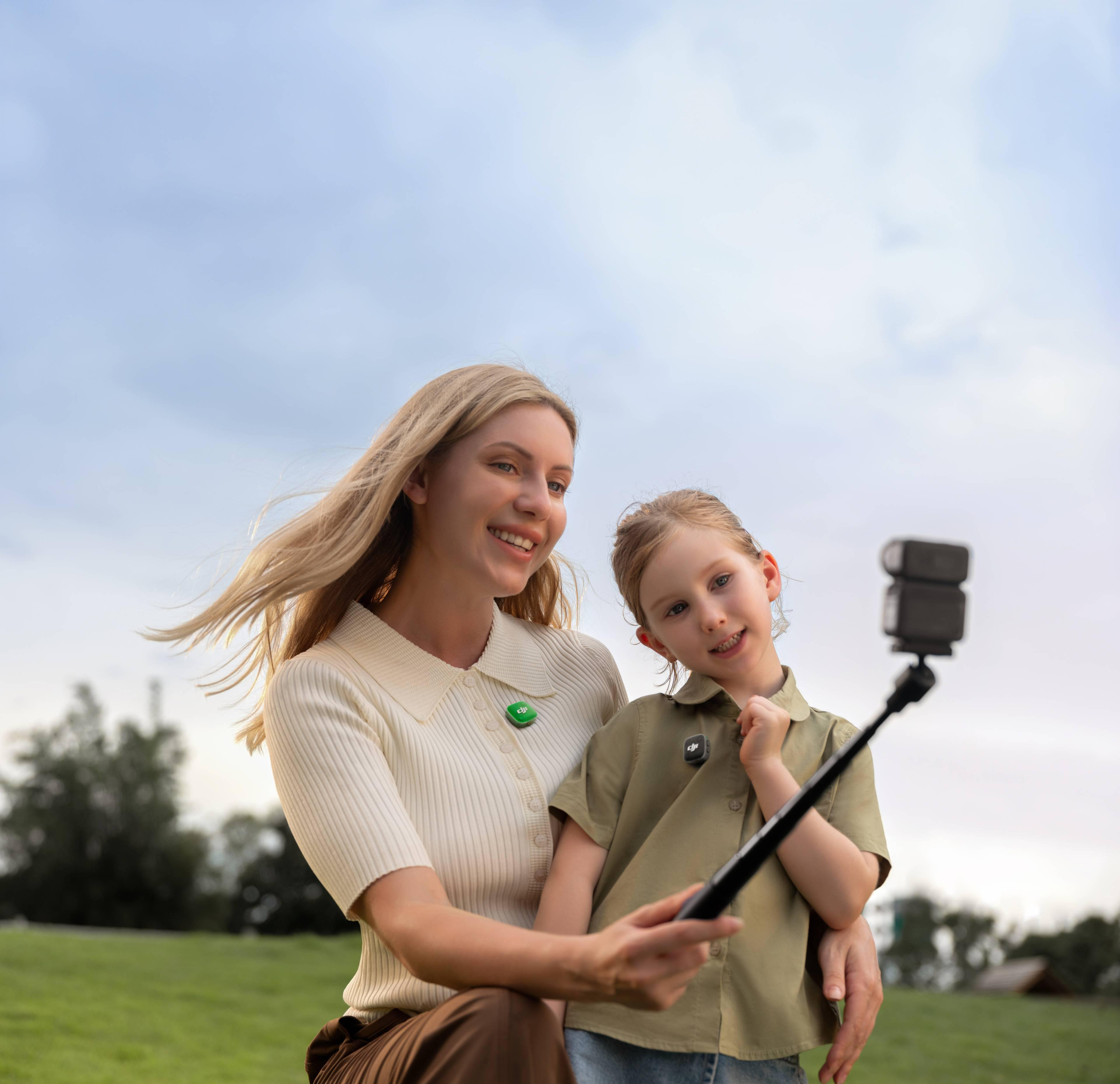 Frau und Kind machen ein Selfie mit einem Selfie-Stick im Freien.