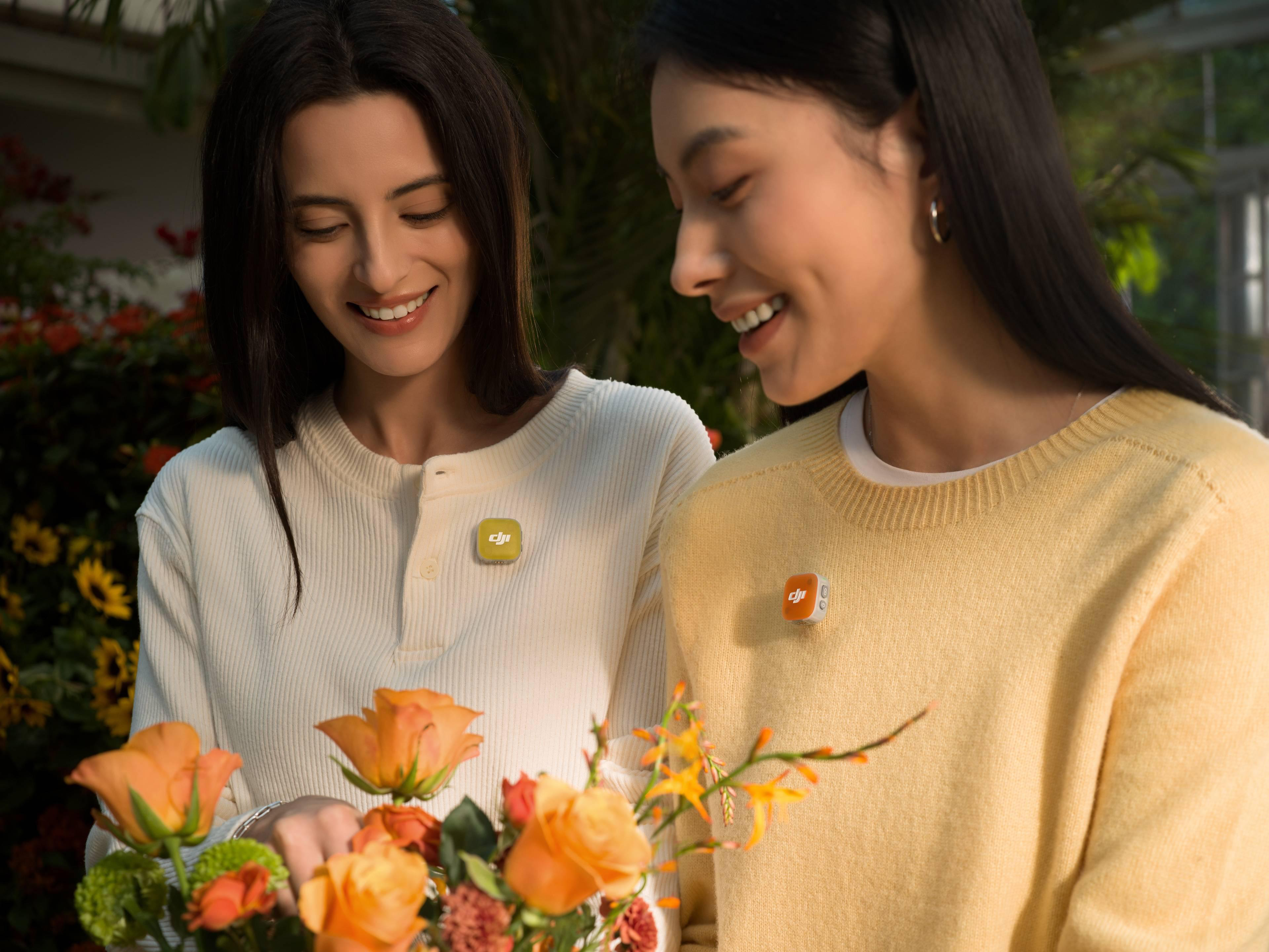 Zwei Frauen lächeln und halten Blumen. Sie tragen Anstecker.