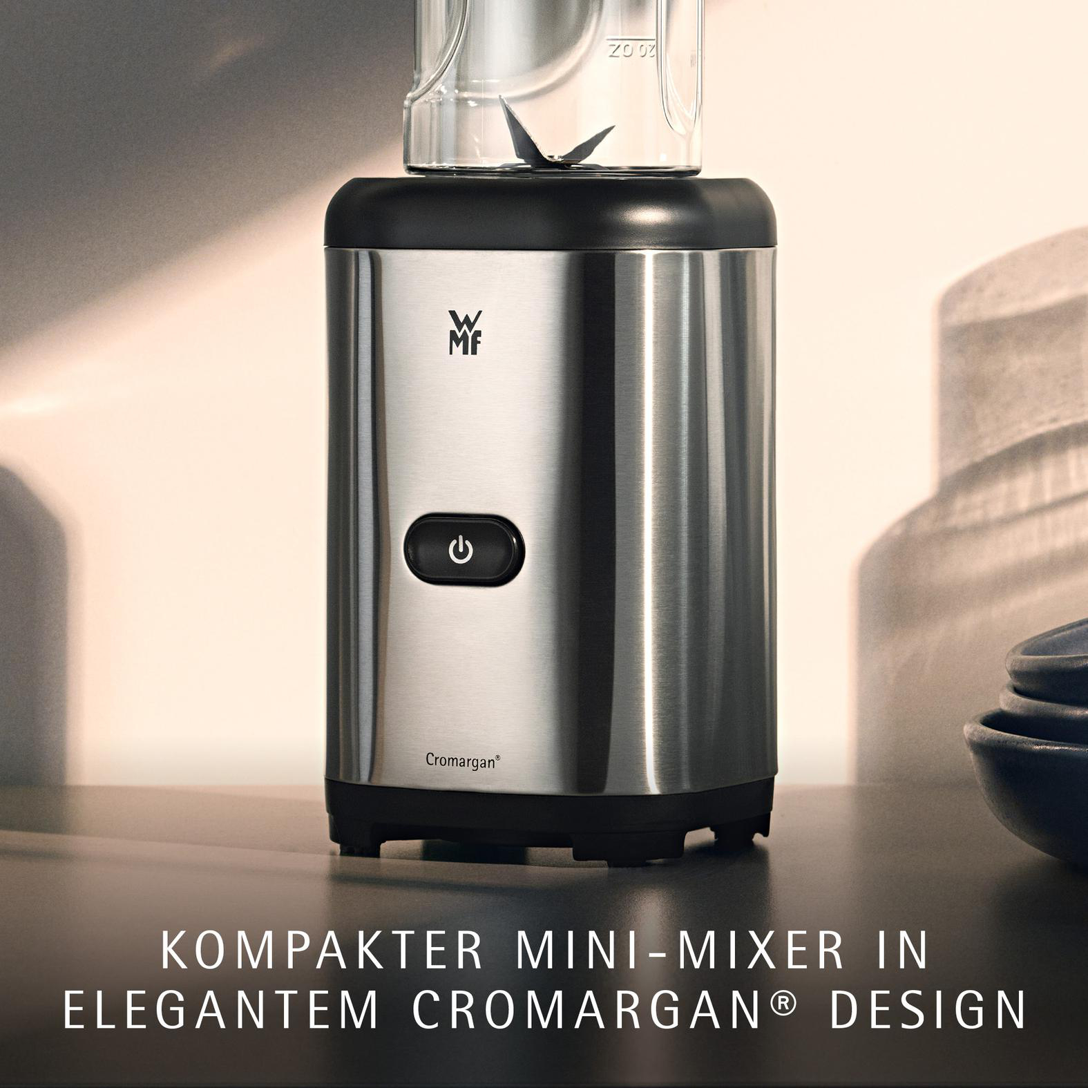 Silberner Mini-Mixer mit schwarzem Knopf, Glasbehälter und Klingen.