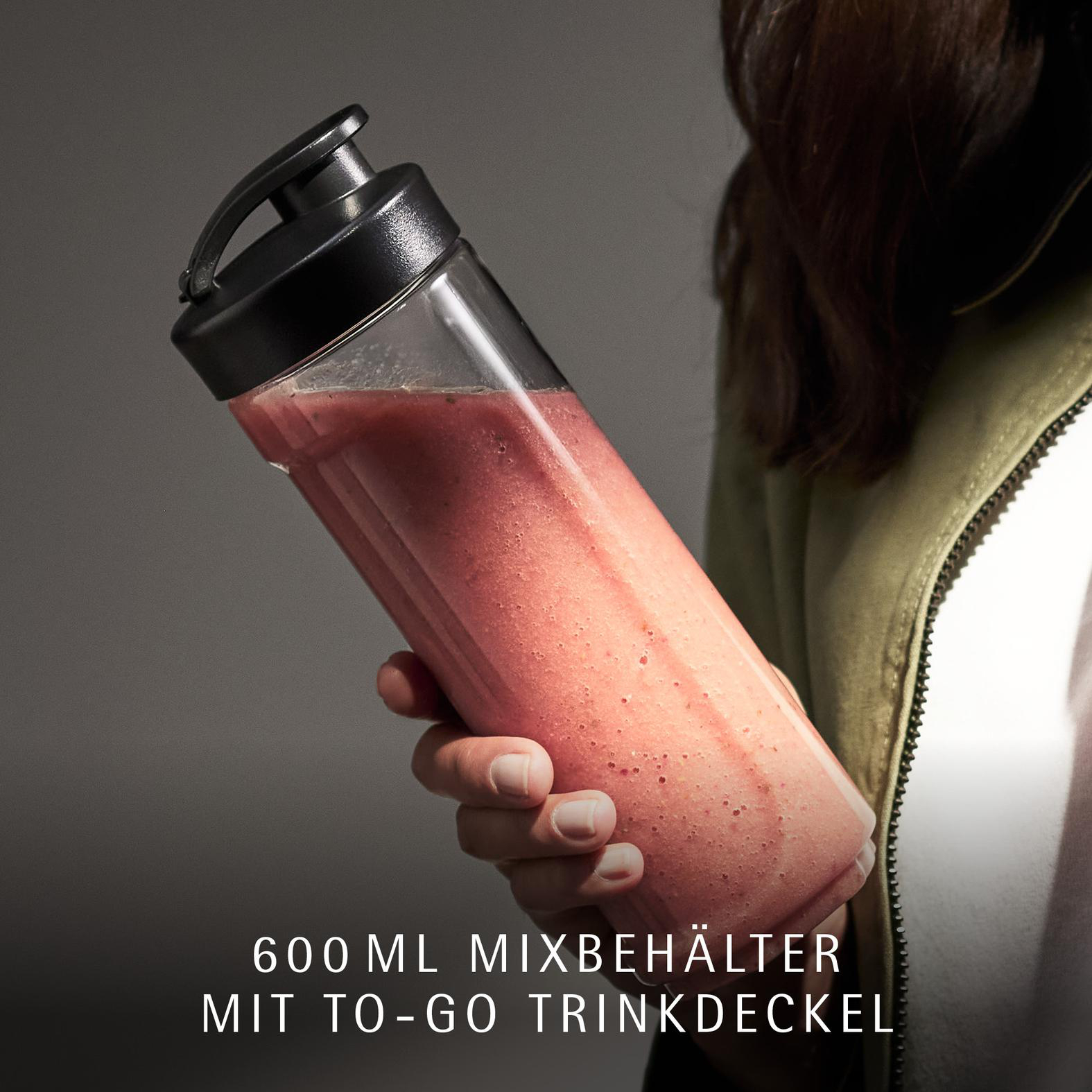 Eine Hand hält einen Mixbehälter mit rotem Smoothie und schwarzem Deckel.