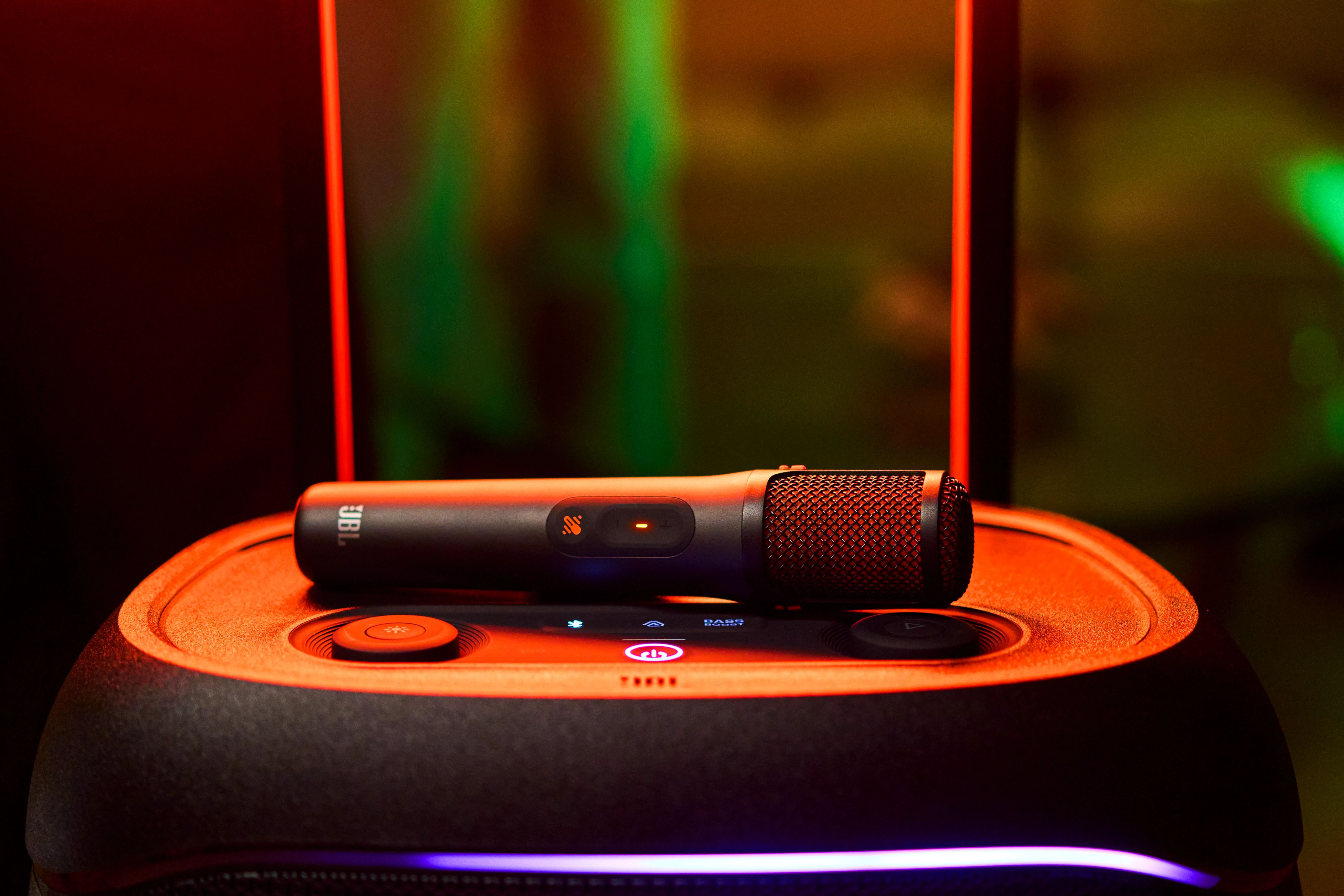 Siyah bir JBL mikrofon, yanıp sönen düğmeleri ve kırmızı ışıkları olan turuncu bir hoparlörün üzerinde duruyor.