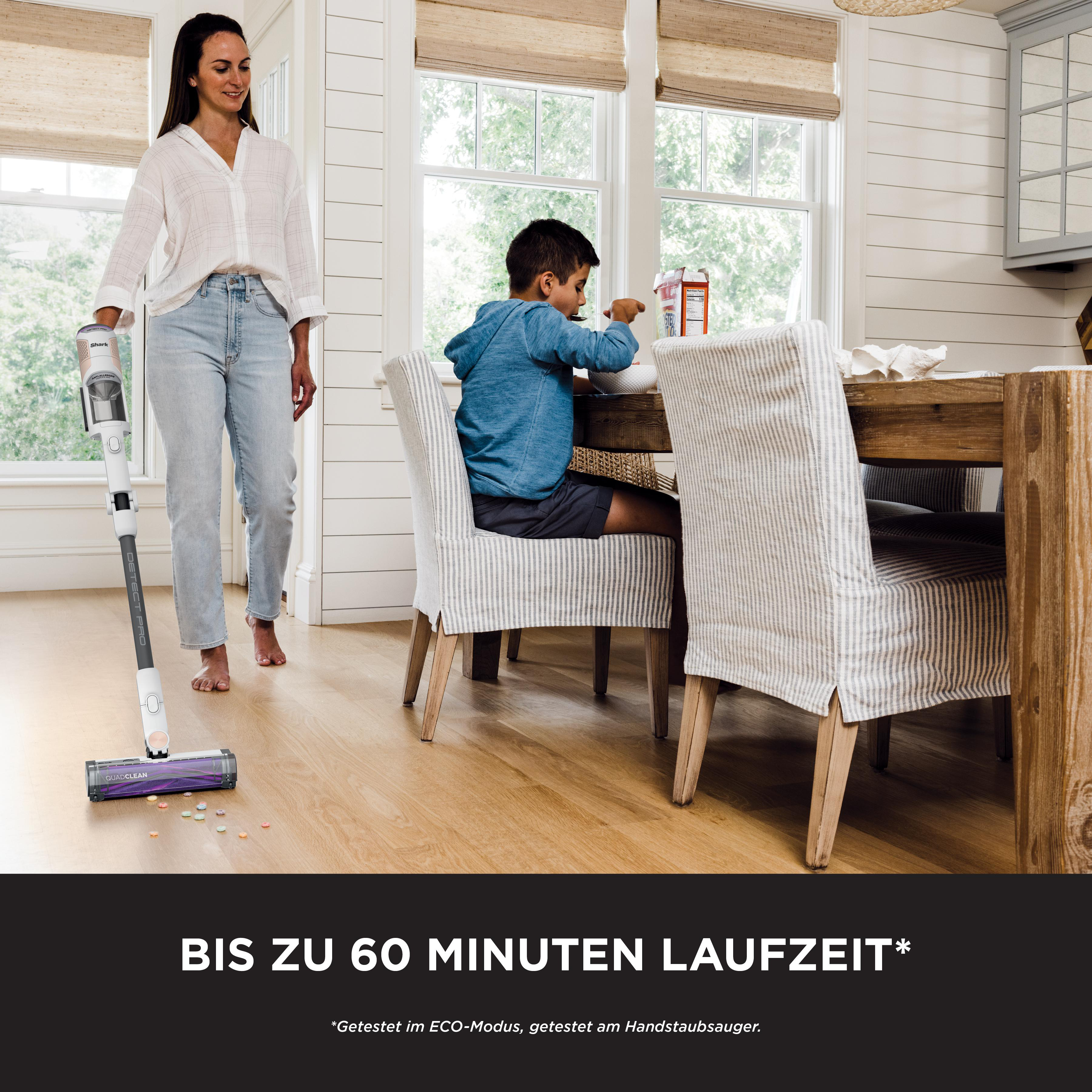 Frau mit Staubsauger und Kind am Tisch in hellem Raum mit Fenstern.
