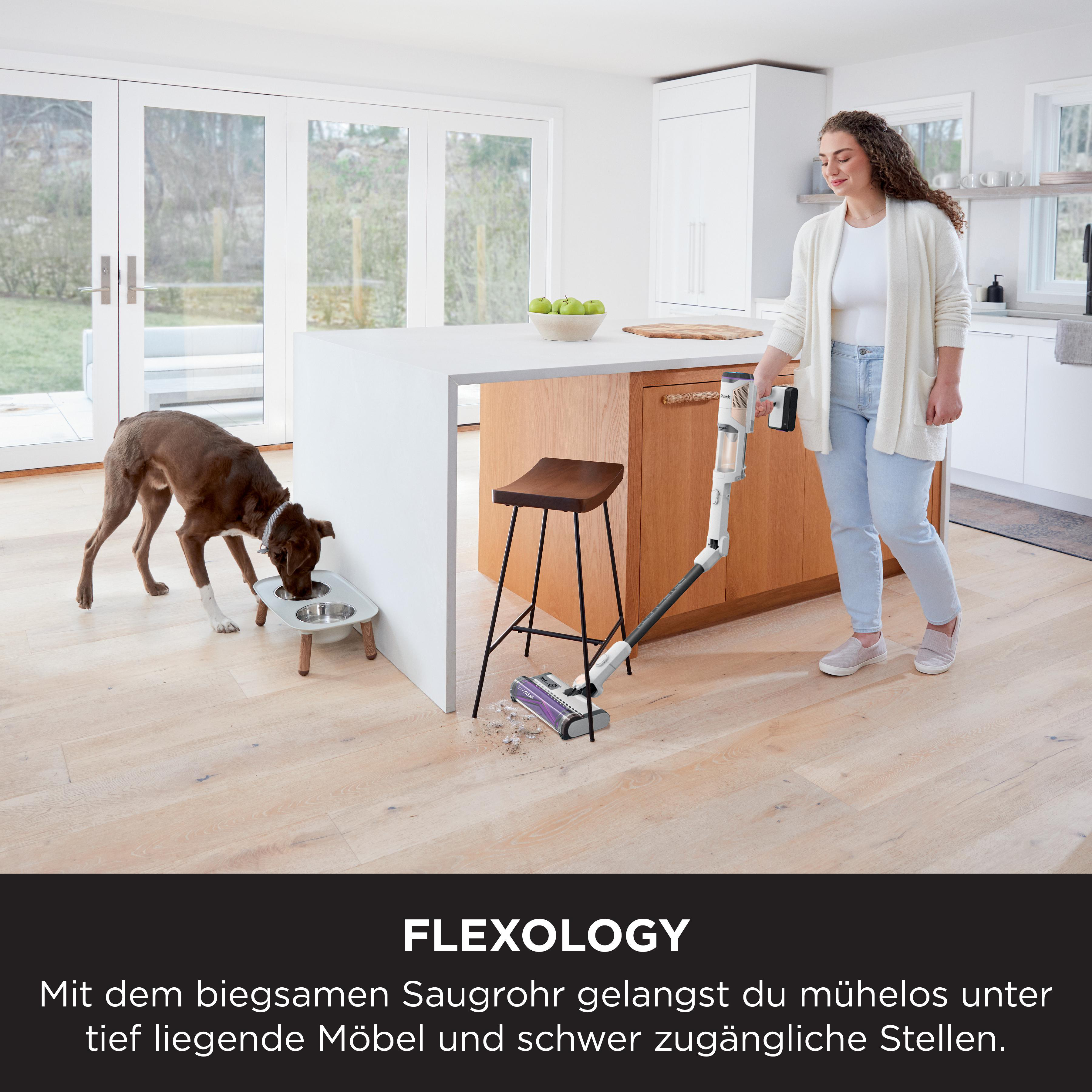 Eine Frau saugt einen Holzboden, während ein Hund frisst. Küchendetails im Hintergrund.