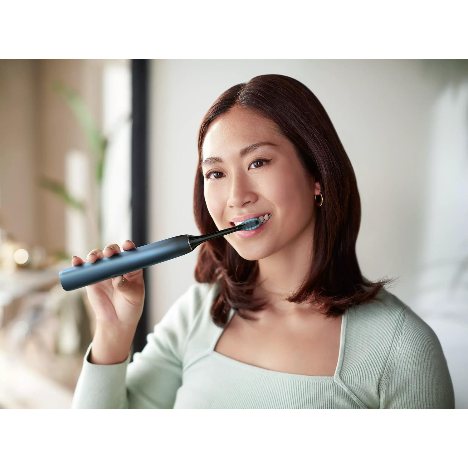 Una donna si lava i denti con uno spazzolino elettrico blu.