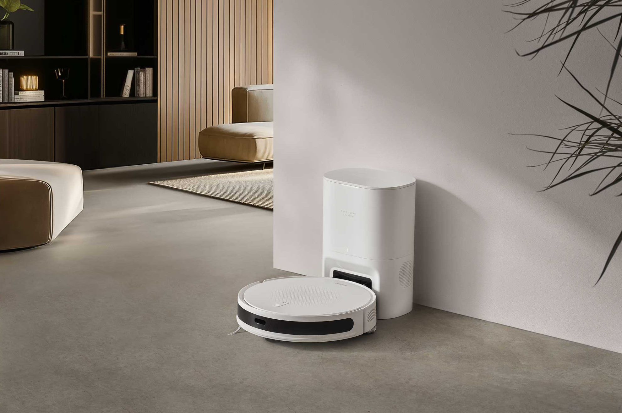Fehér robotporszívó töltőállomással szürke padlón. Bútorok a háttérben.