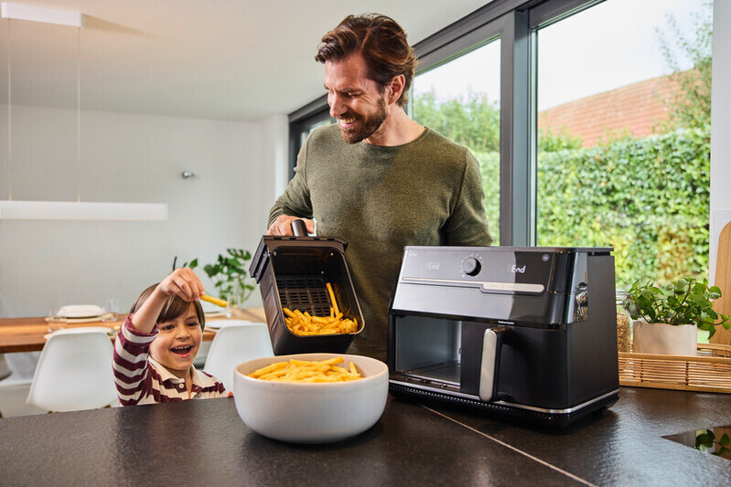 Homme et enfant avec frites près d'une friteuse à air dans une cuisine moderne.