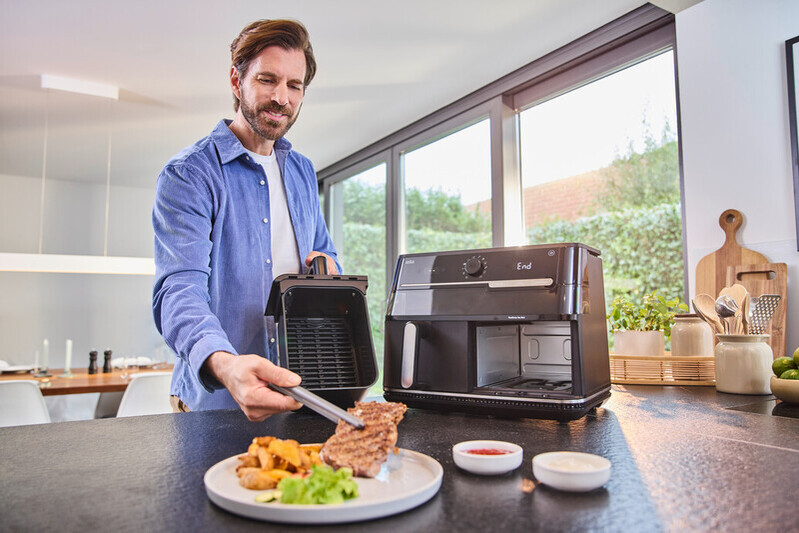Un homme met un steak dans une friteuse à air. Assiette avec frites et salade.