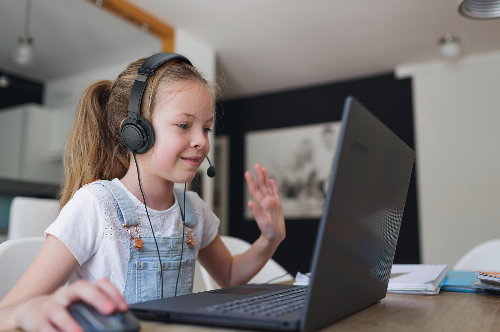 Egy lány fejhallgatóval integet egy laptopnak.