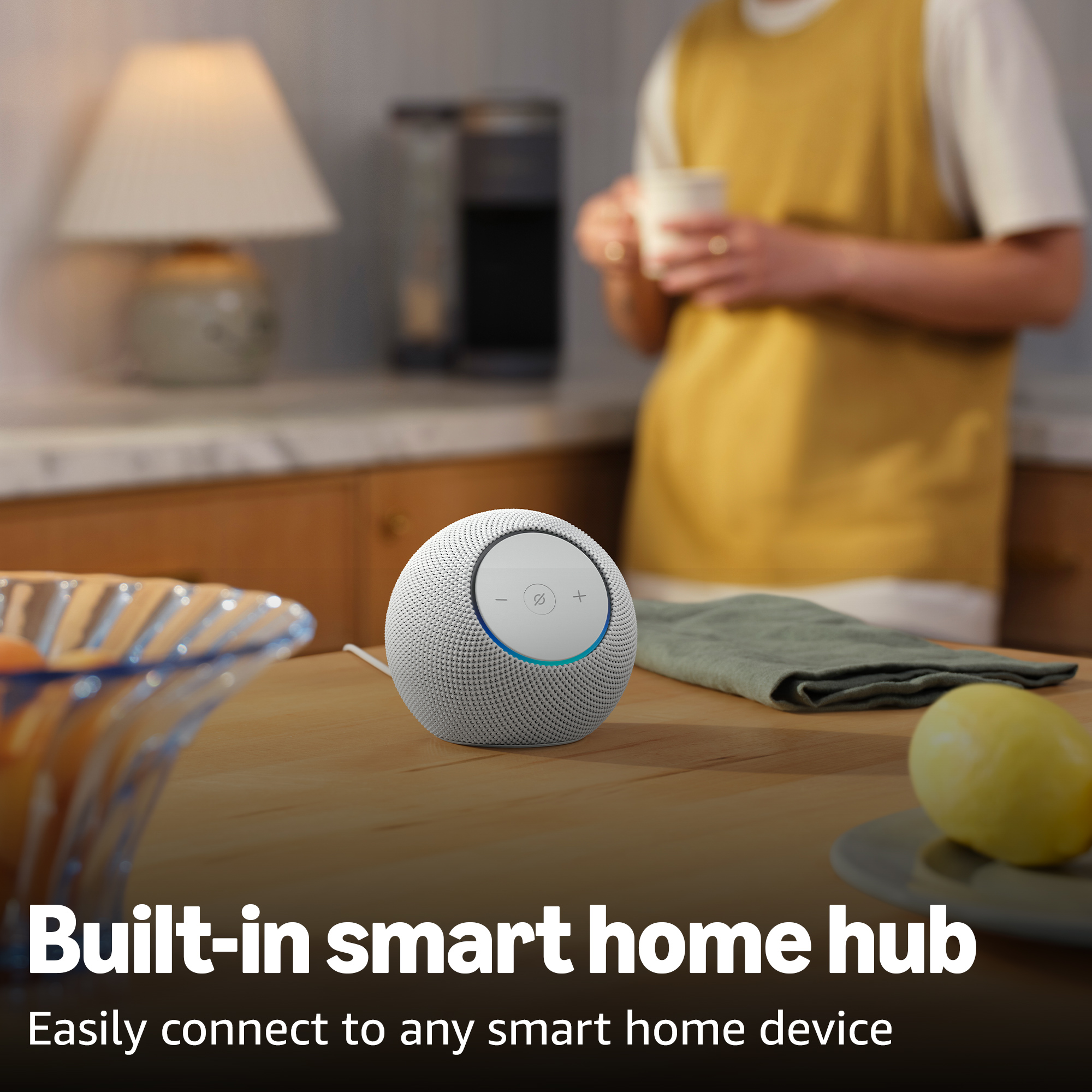 Un altoparlante smart bianco su un tavolo di legno, vicino a una ciotola di frutta e un limone.