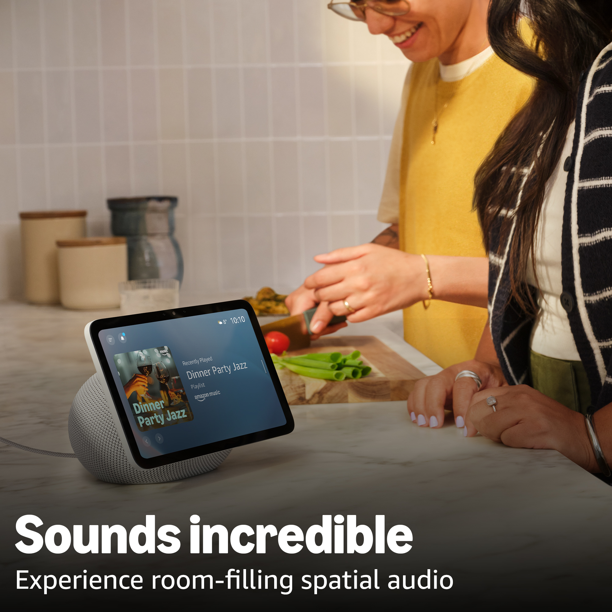 Ein Smart Speaker mit Tablet spielt Jazz. Zwei Personen bereiten Essen zu.