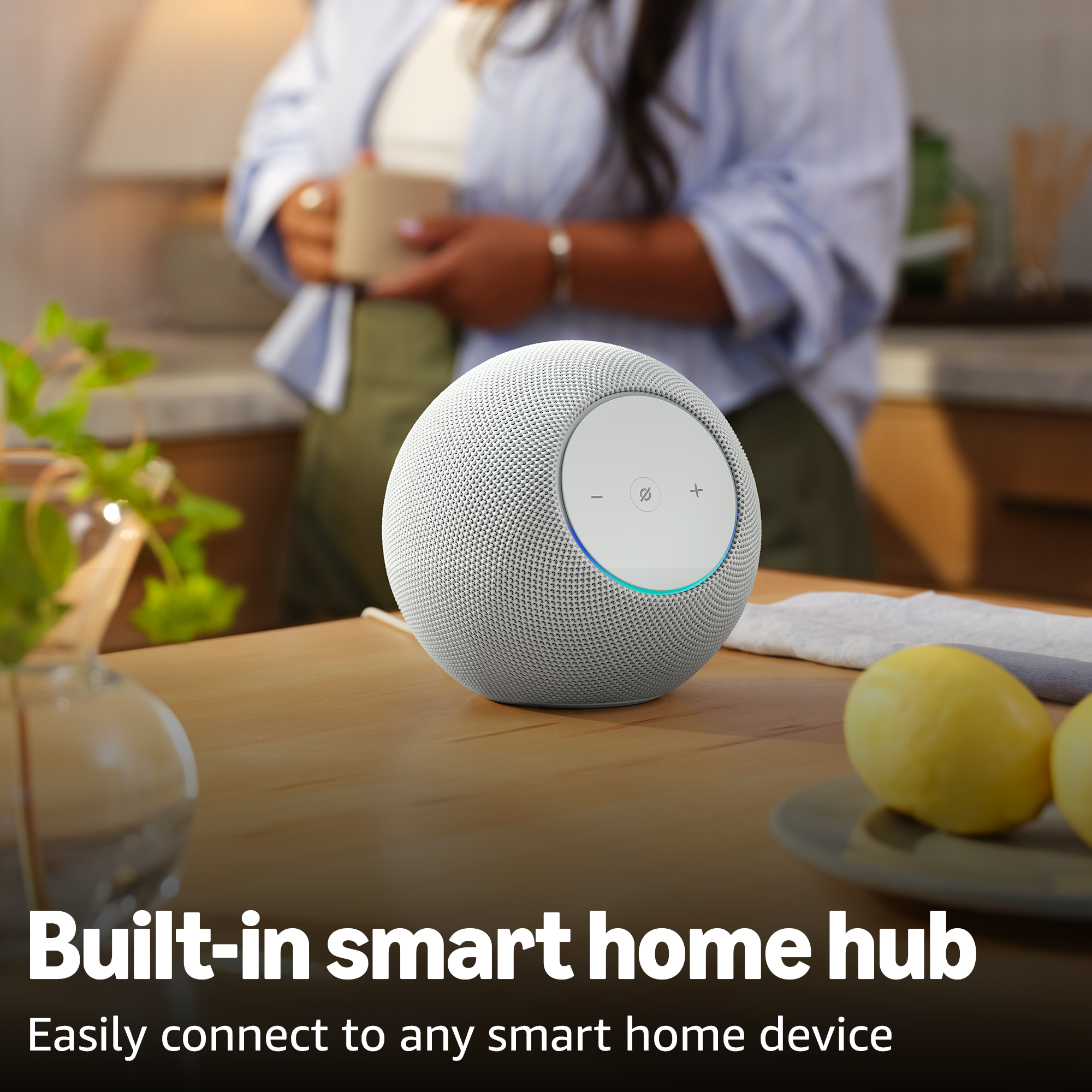 Ein weißer Smart Speaker steht auf einem Holztisch mit Zitronen und einer Frau im Hintergrund.