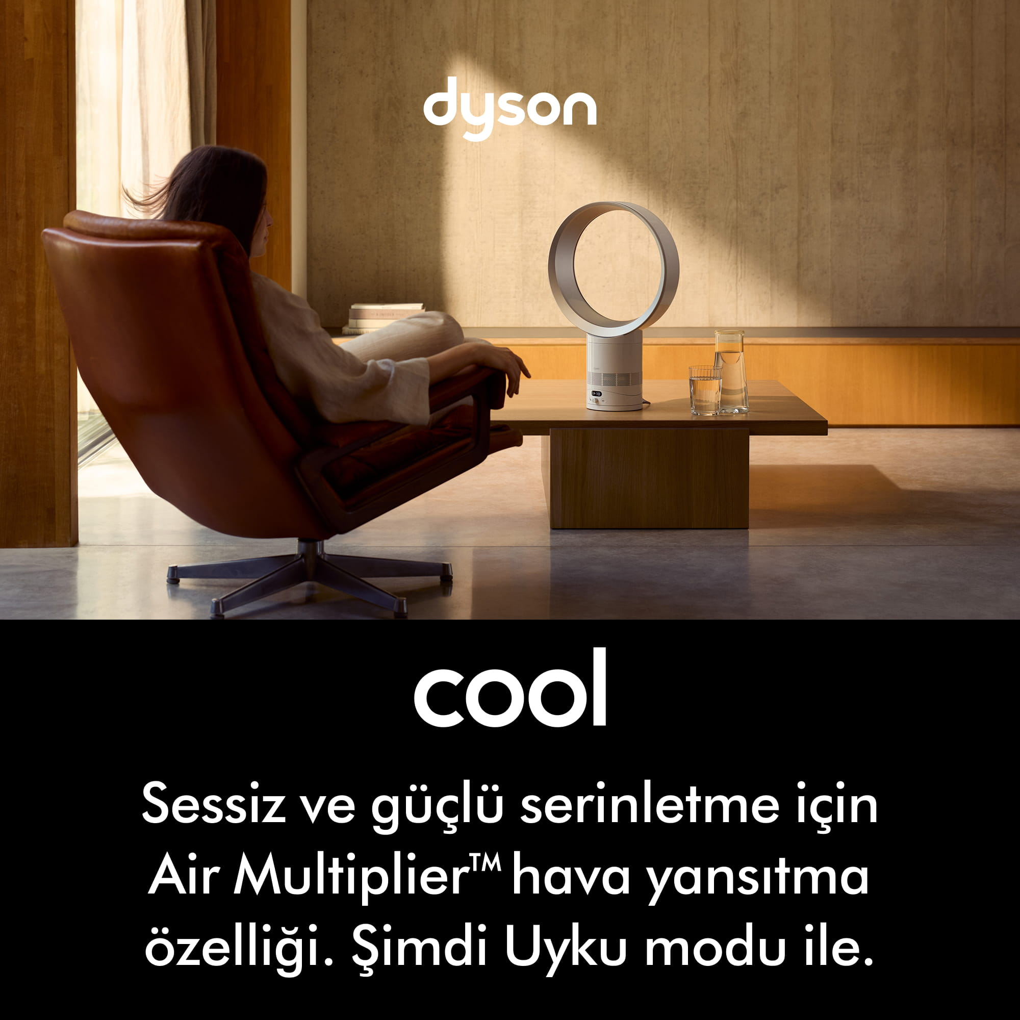 Bir kadın Dyson vantilatör önünde deri koltukta oturuyor.