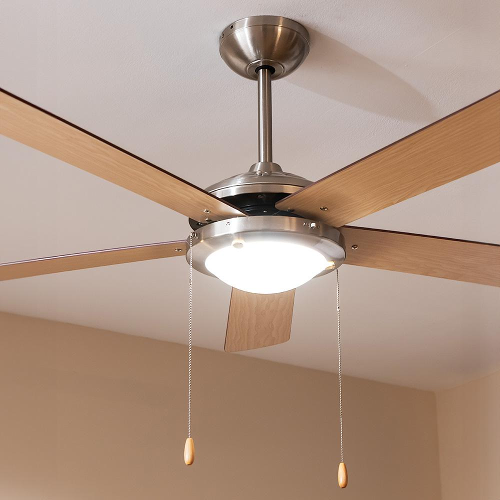 Un ventilador de techo moderno con cinco aspas de madera y acabado metálico cepillado, iluminado por una luz central.