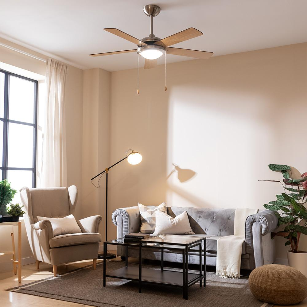 Una sala de estar con sofá gris, sillón, mesa de centro, lámpara de pie y ventilador de techo.