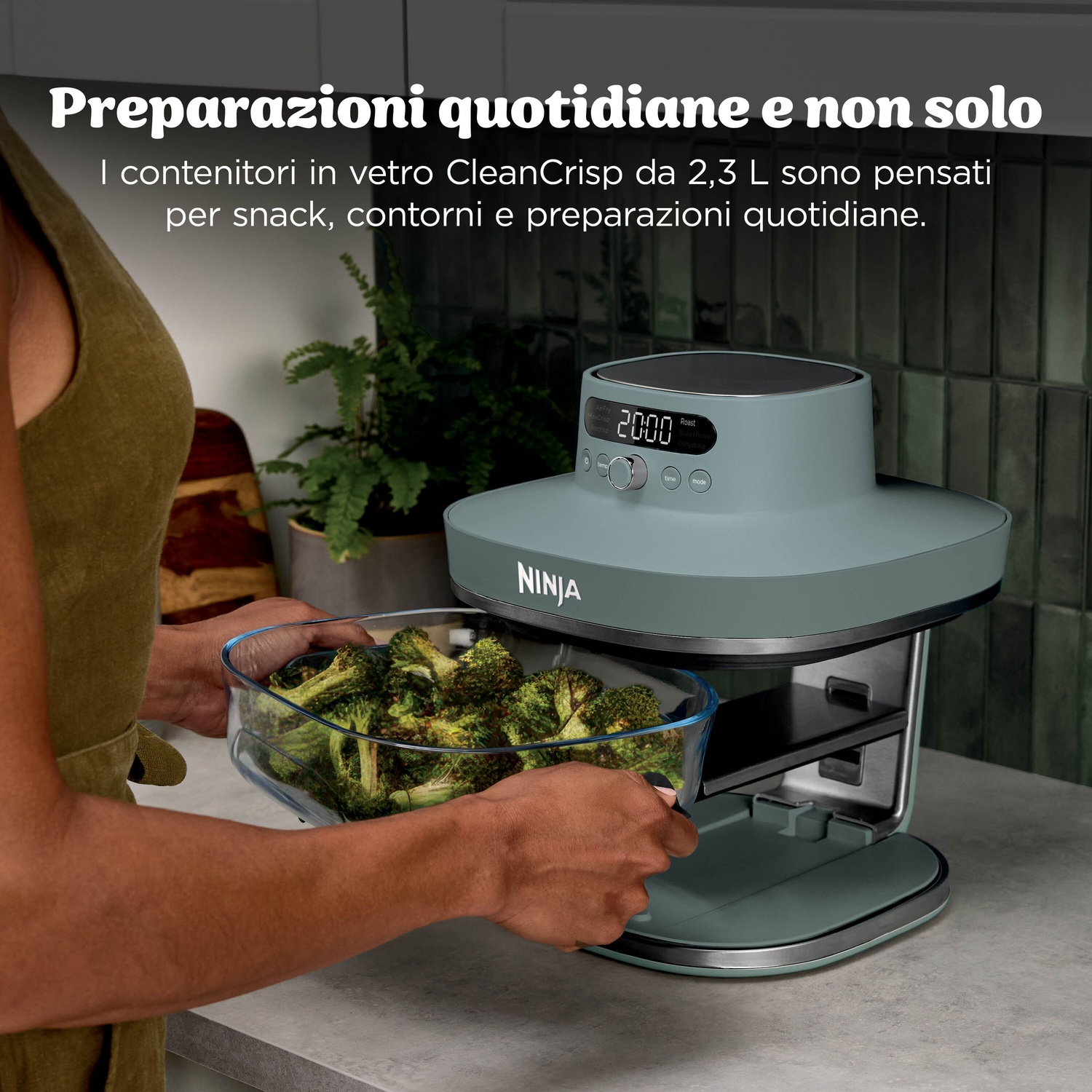 Una persona mette una ciotola di vetro di broccoli in un forno friggitrice ad aria Ninja grigio.