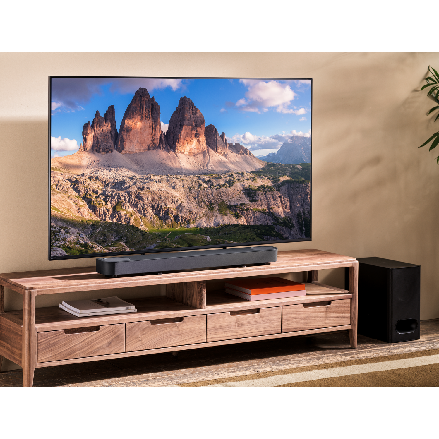 A TV displays a mountain landscape. Below it, a wooden cabinet with a soundbar and subwoofer.