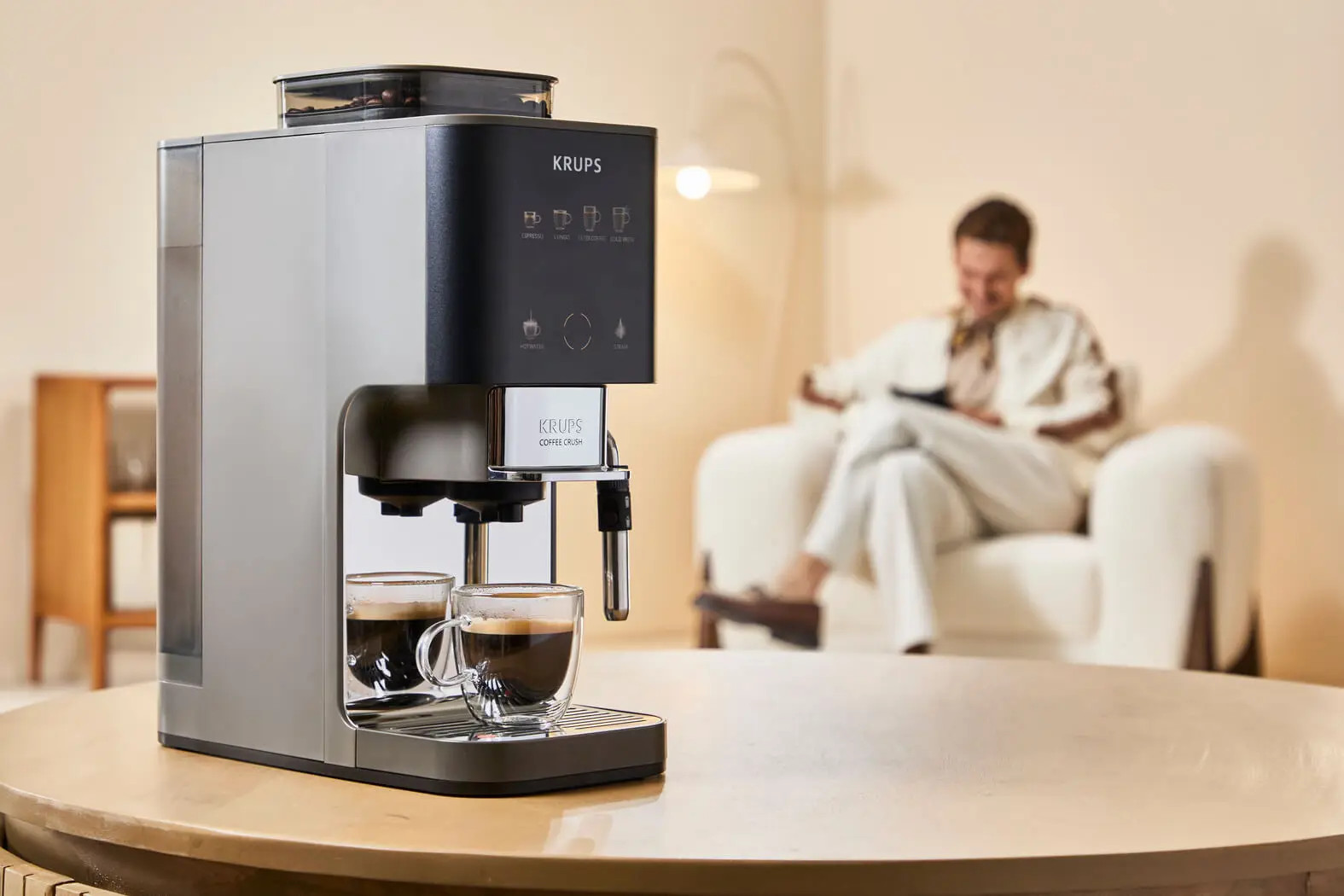 Ekspres do kawy Krups z dwoma filiżankami espresso, mężczyzna siedzi w tle.