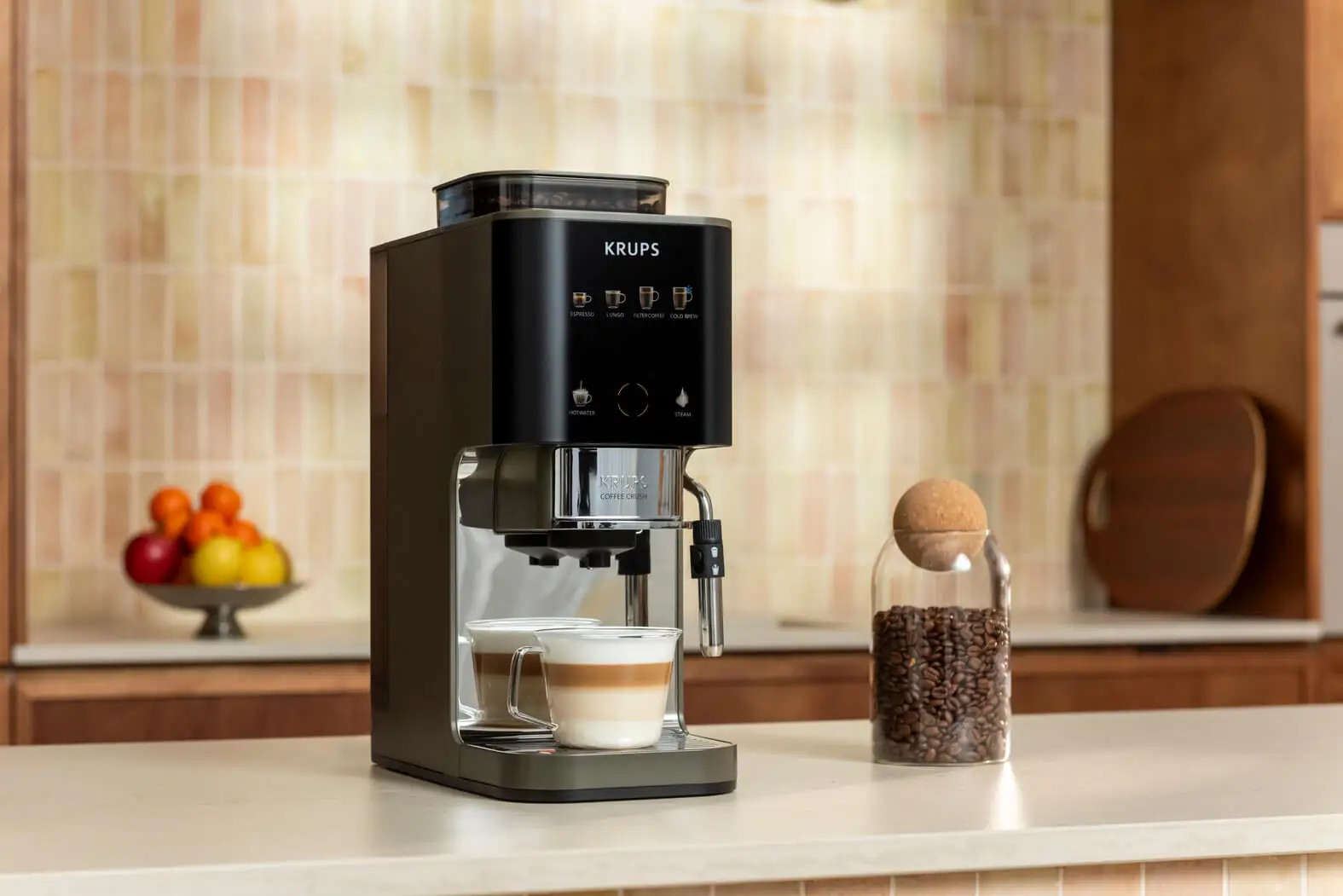 Czarny ekspres do kawy KRUPS z dwoma filiżankami cappuccino i karafką z ziaren kawy.