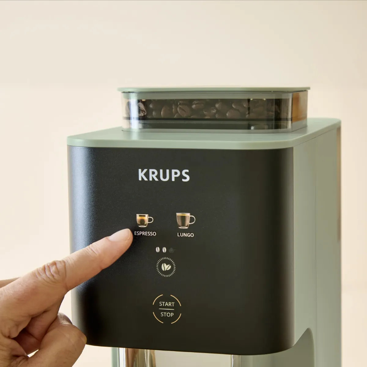 Ręka naciska przycisk ESPRESSO na ekspresie KRUPS z zasobnikiem na ziarna.
