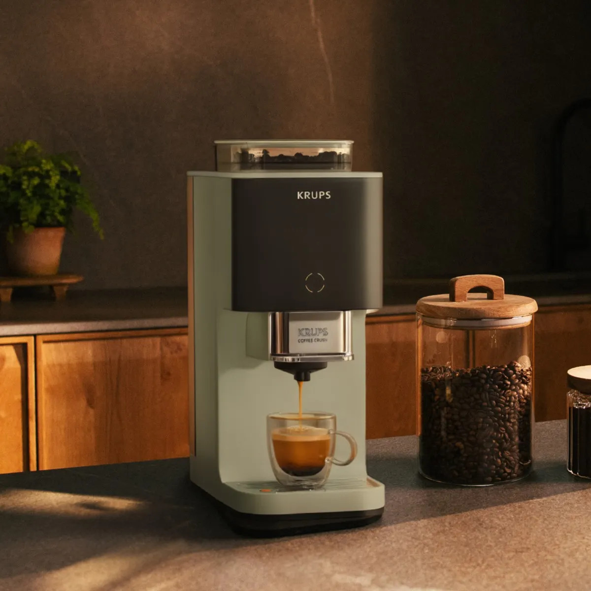 Ekspres do kawy Krups parzy espresso do szklanki, obok słój z ziarnami kawy.