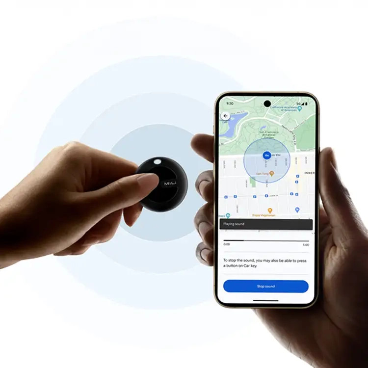 Jedna ręka trzyma czarny lokalizator Mili, druga ręka trzyma telefon z mapą i niebieskim okręgiem.