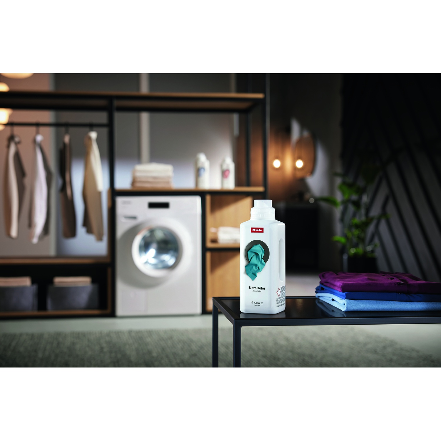 Lavanderia con detersivo Miele UltraColor, lavatrice e abiti piegati.