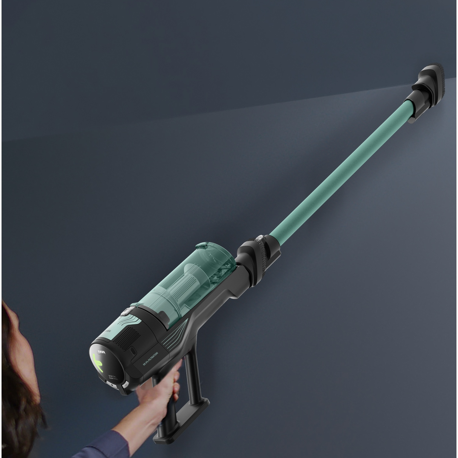 A person holds a black and green cordless vacuum cleaner pointed at a wall.