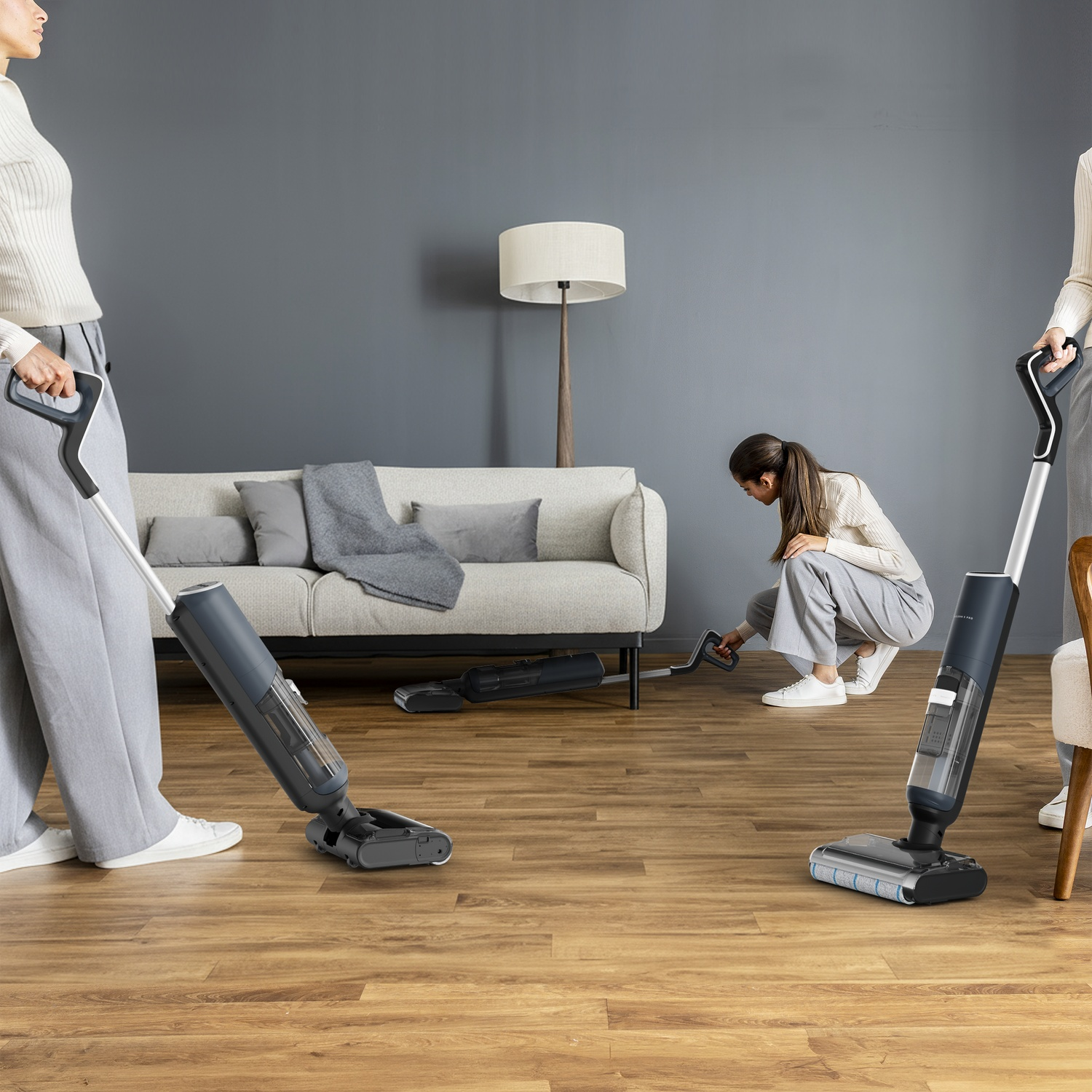 People cleaning a wooden floor with cordless vacuum cleaners in a modern living room.