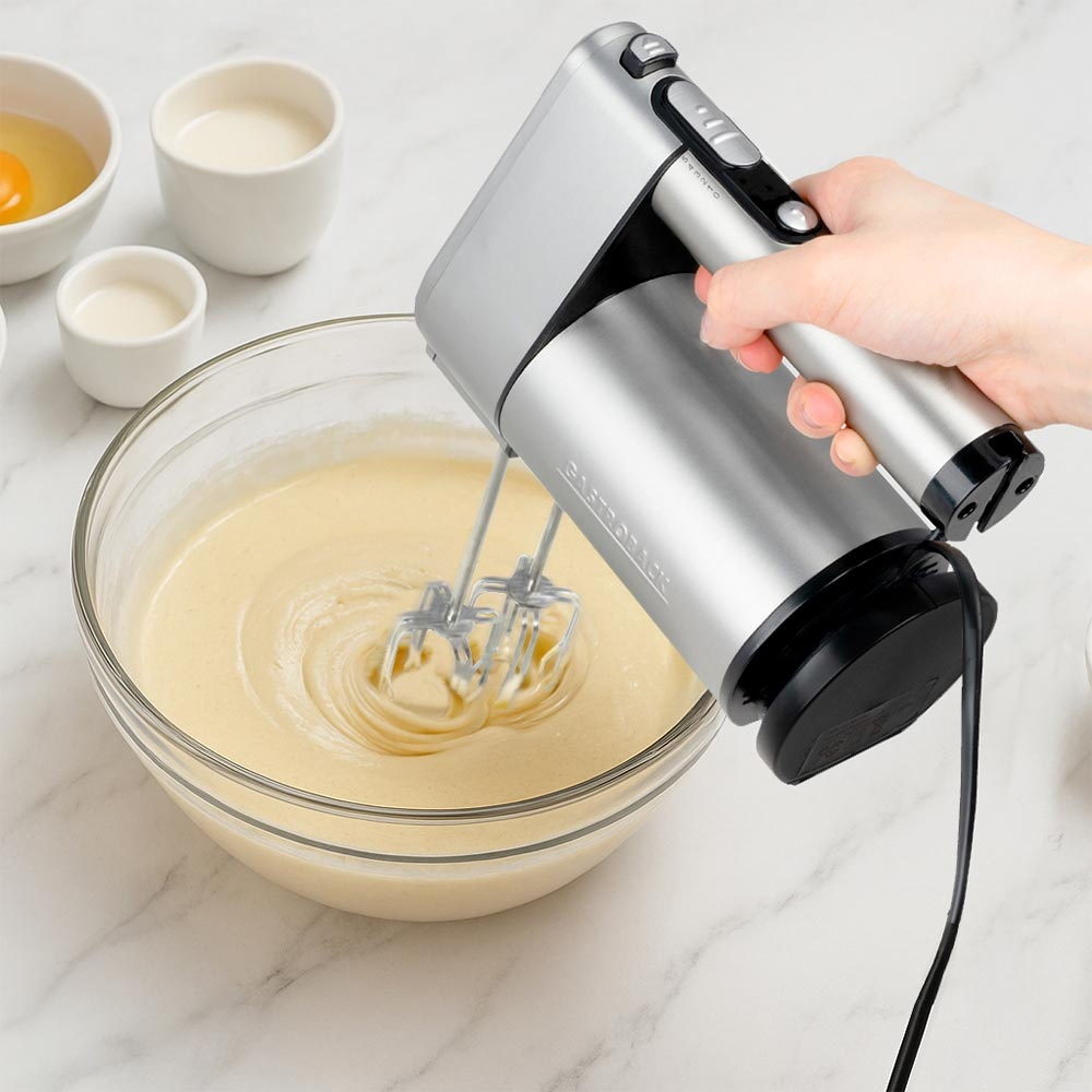 Handmixer mixt Teig in einer Glasschüssel, neben Zutaten in weißen Schalen.