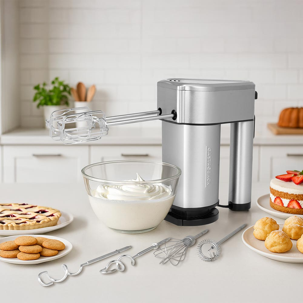 Ein silberner Handmixer mit Zubehör, Schüssel mit Sahne, Kuchen und Keksen.