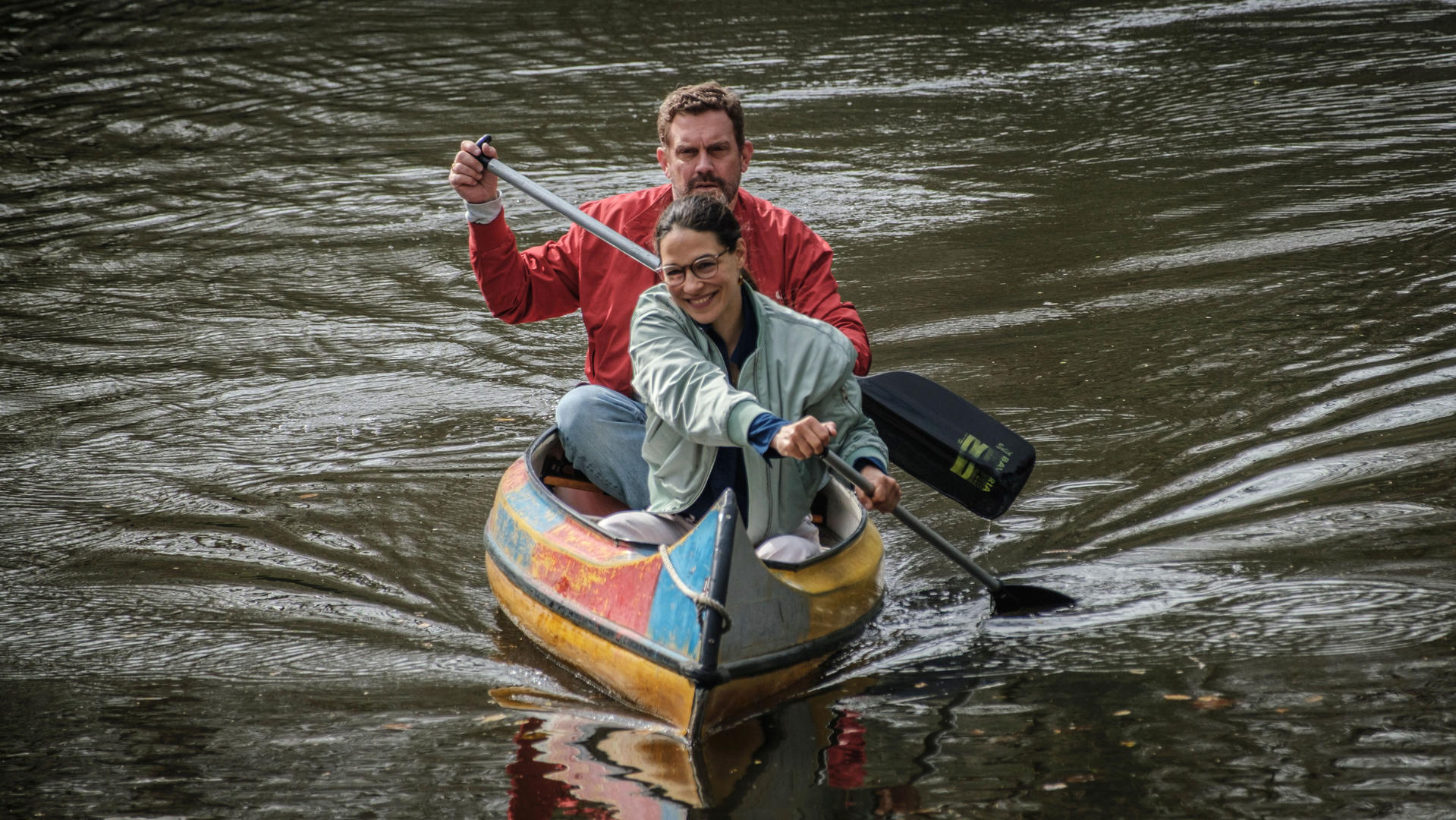 Mann und Frau rudern in einem bunten Kanu auf einem Fluss.