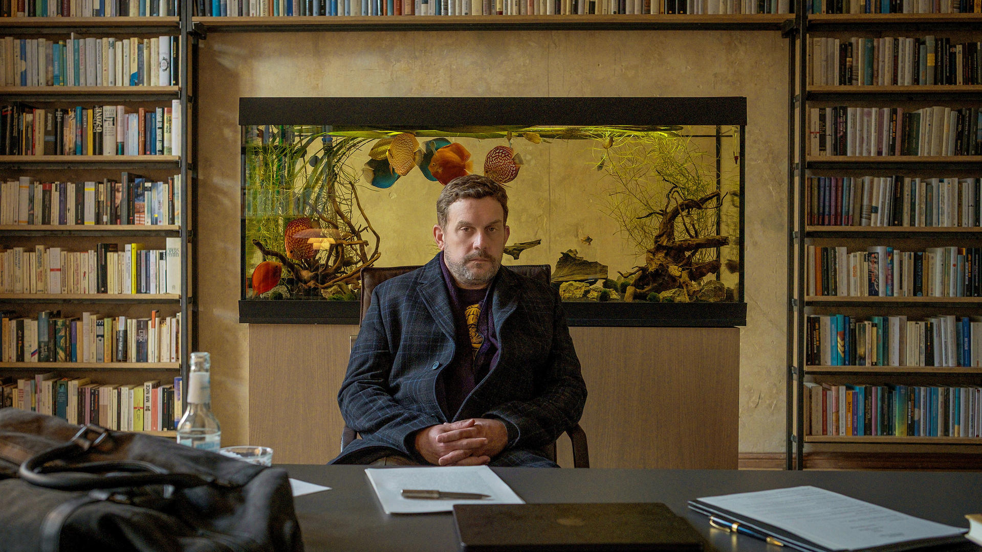 Mann sitzt vor Aquarium und Bücherregalen.