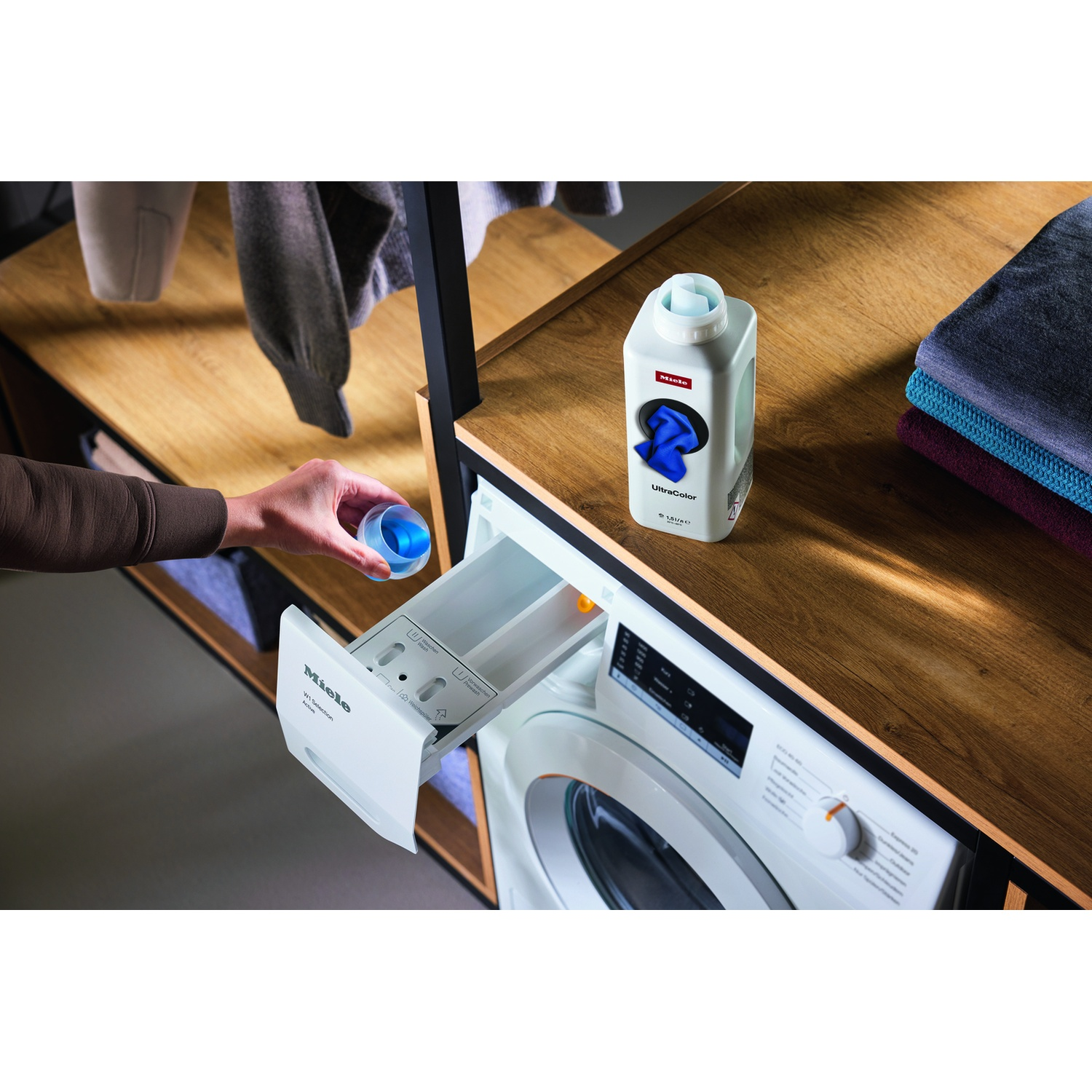 Una mano aggiunge liquido blu al cassetto detersivo di una lavatrice Miele.