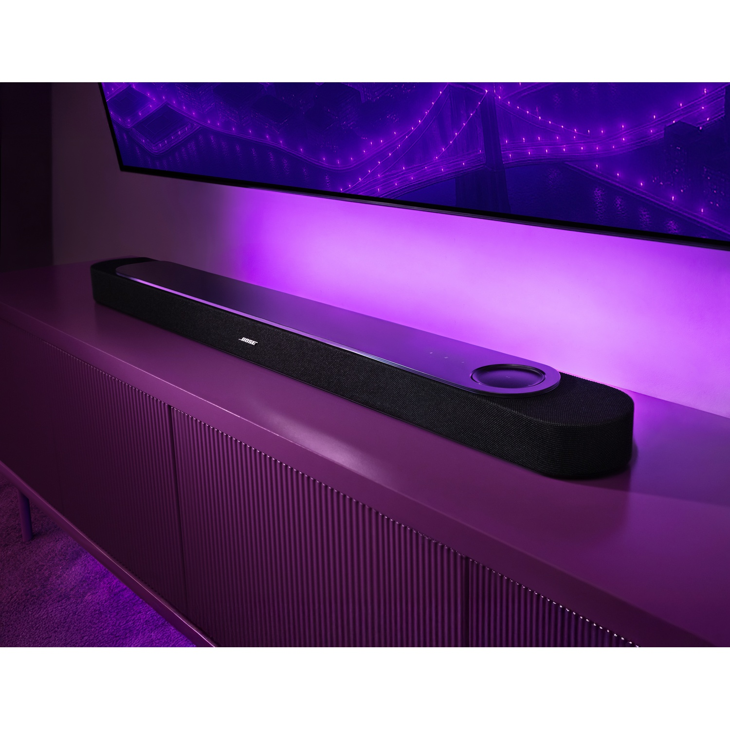 Soundbar nera su un mobile viola sotto un televisore con illuminazione viola.